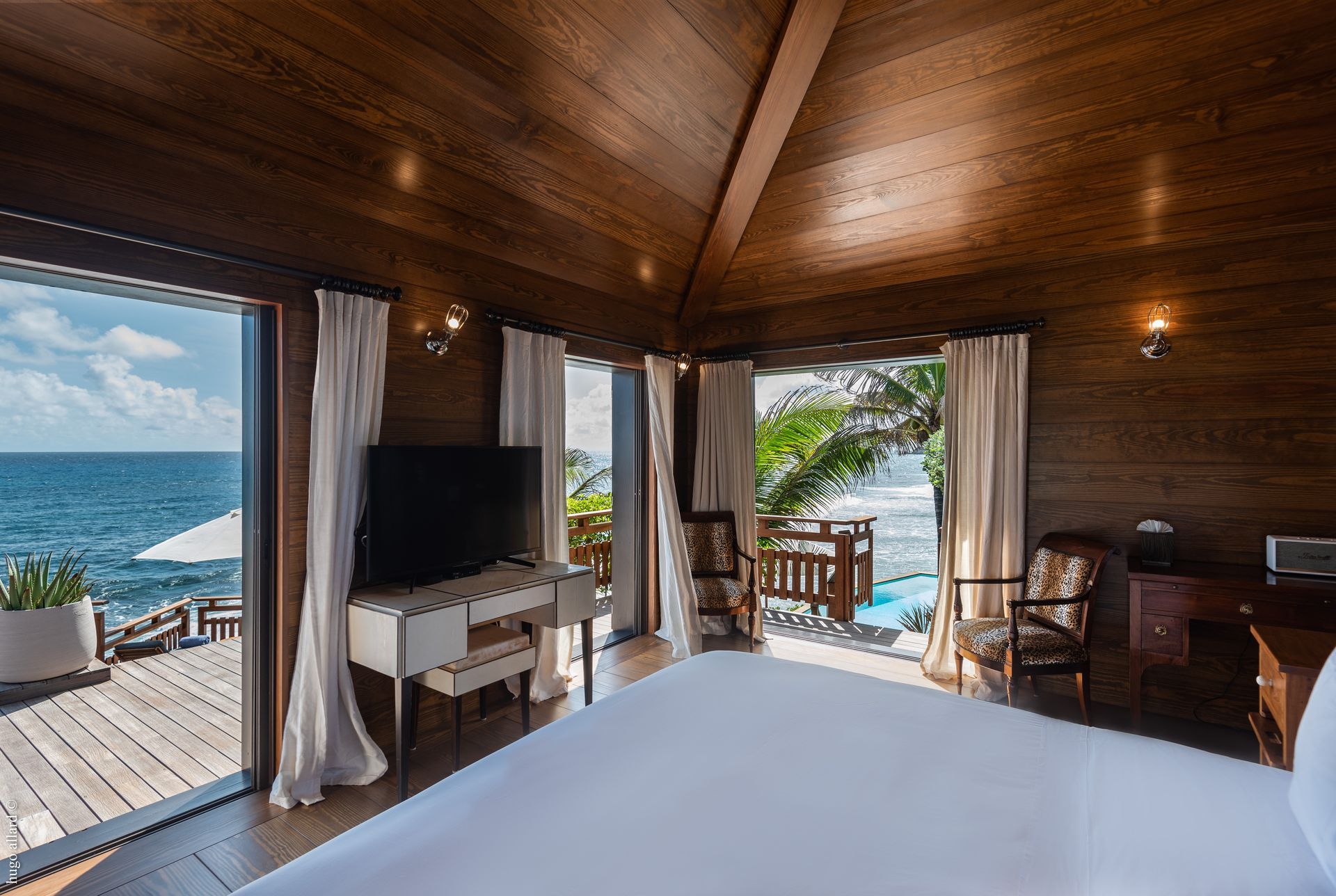 a hotel room with a bed, television, chairs and a view of the ocean