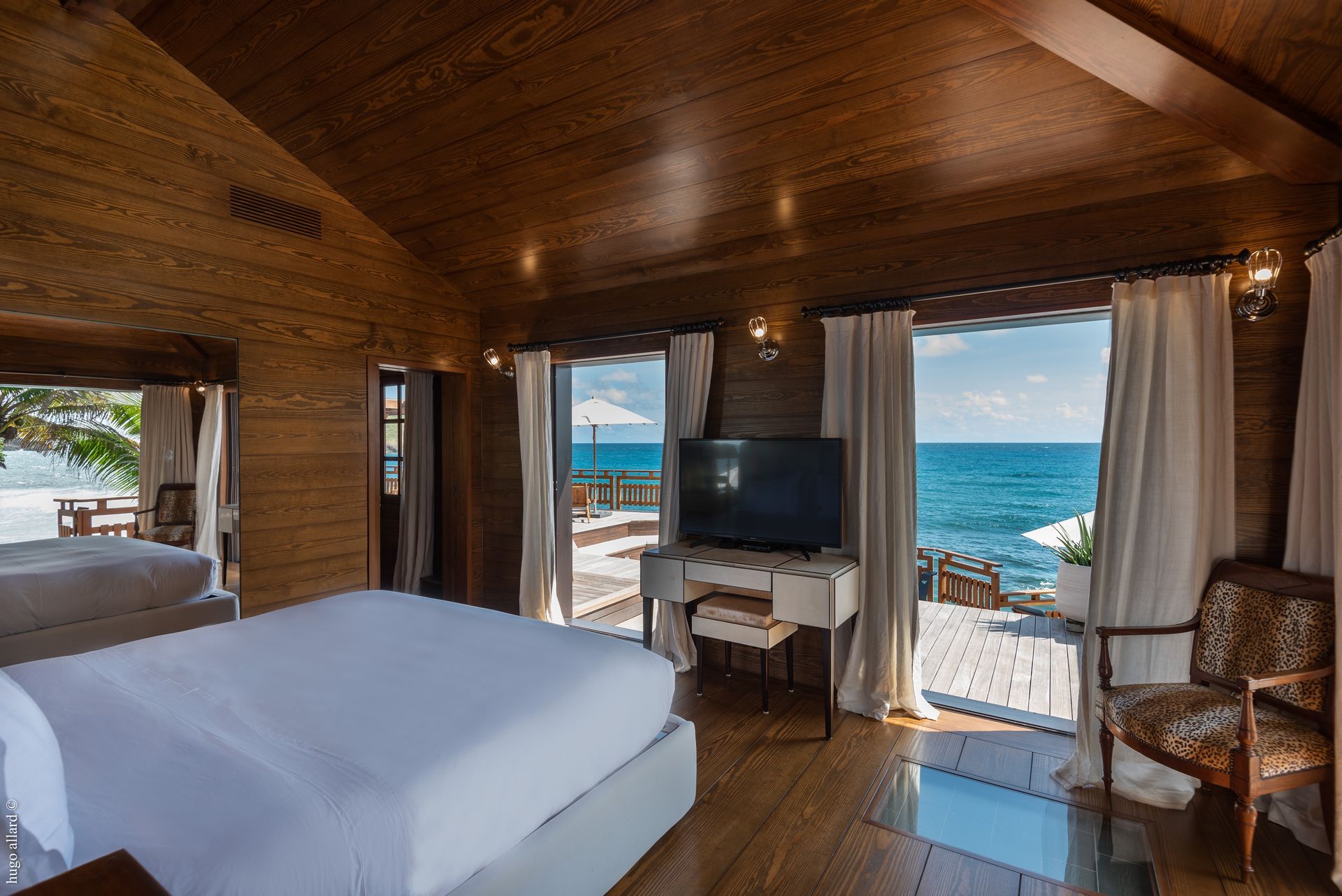 a hotel room with a bed, chair, television and a view of the ocean