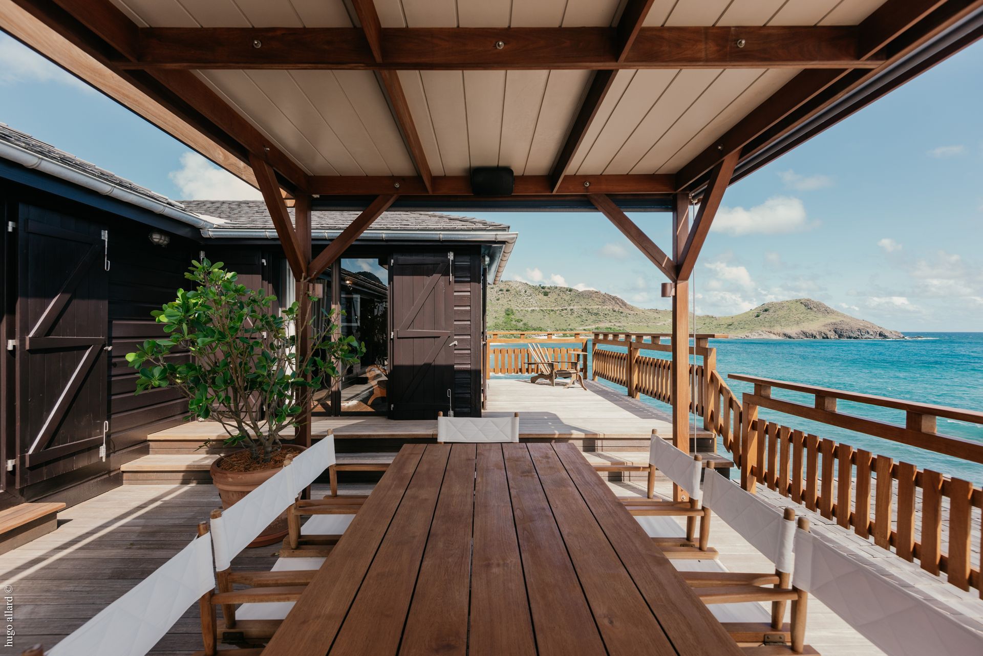 a wooden table and chairs under a canopy overlooking the ocean