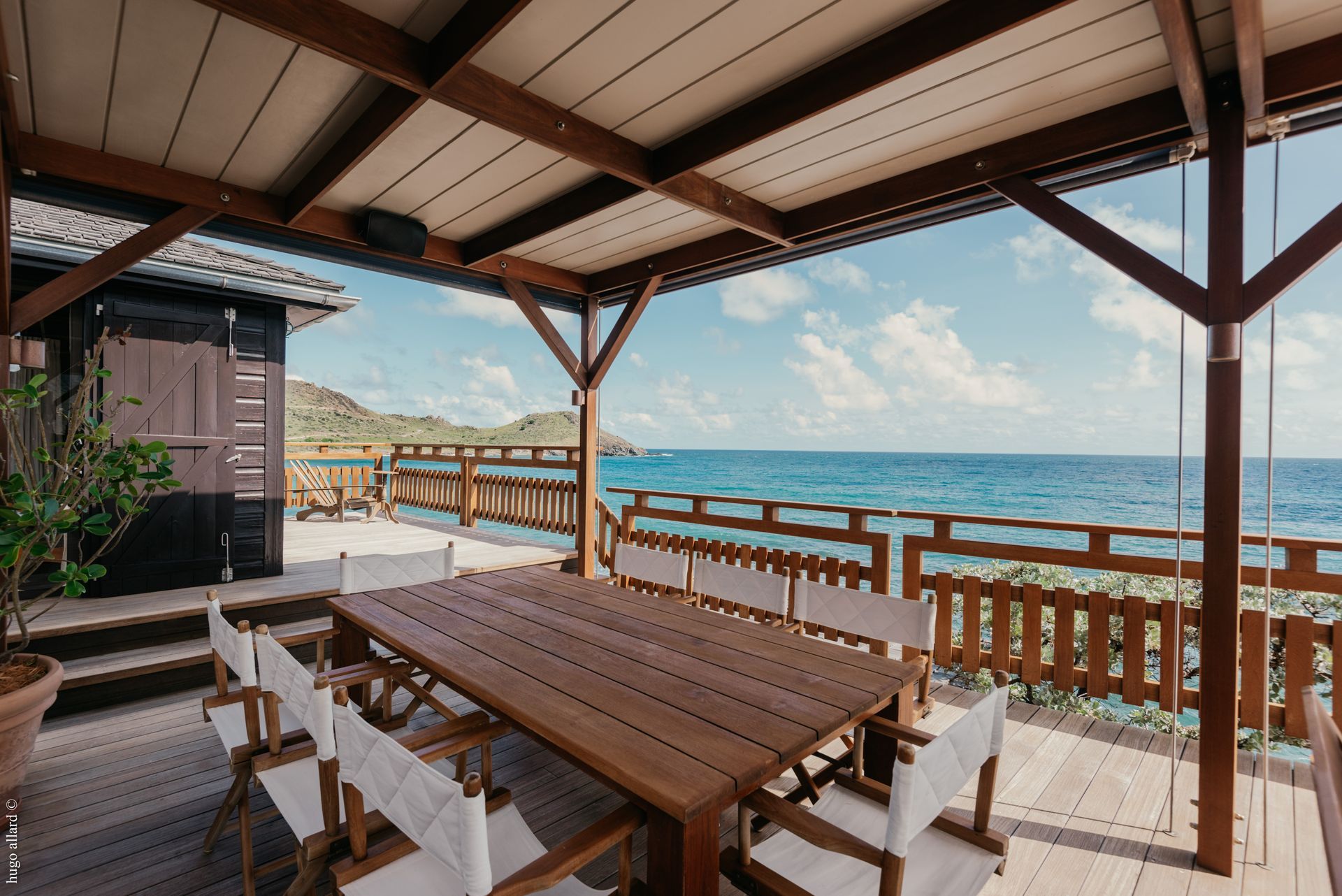 a wooden table and chairs on a deck overlooking the ocean