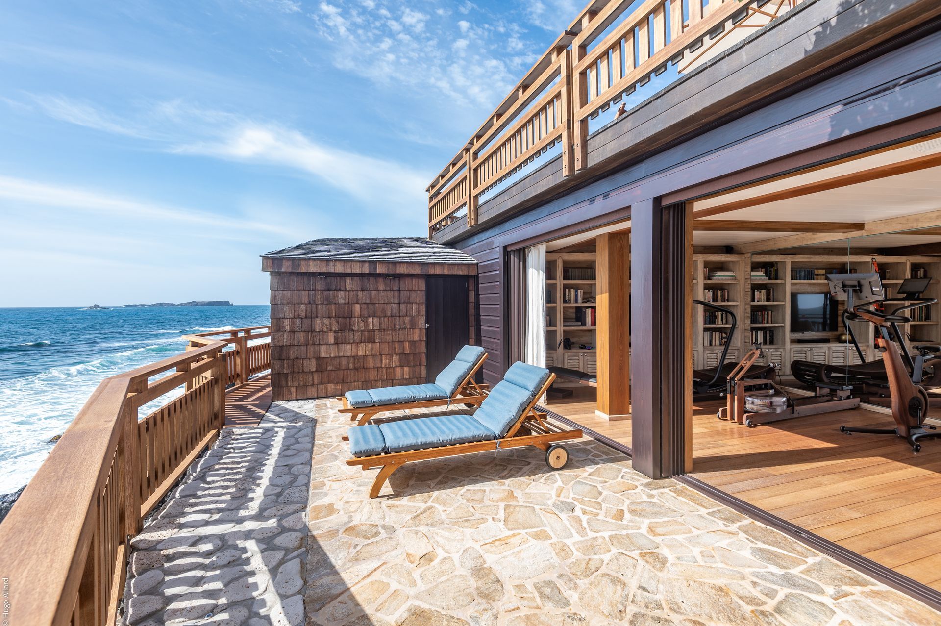there are two lounge chairs on the balcony of a house with a view of the ocean