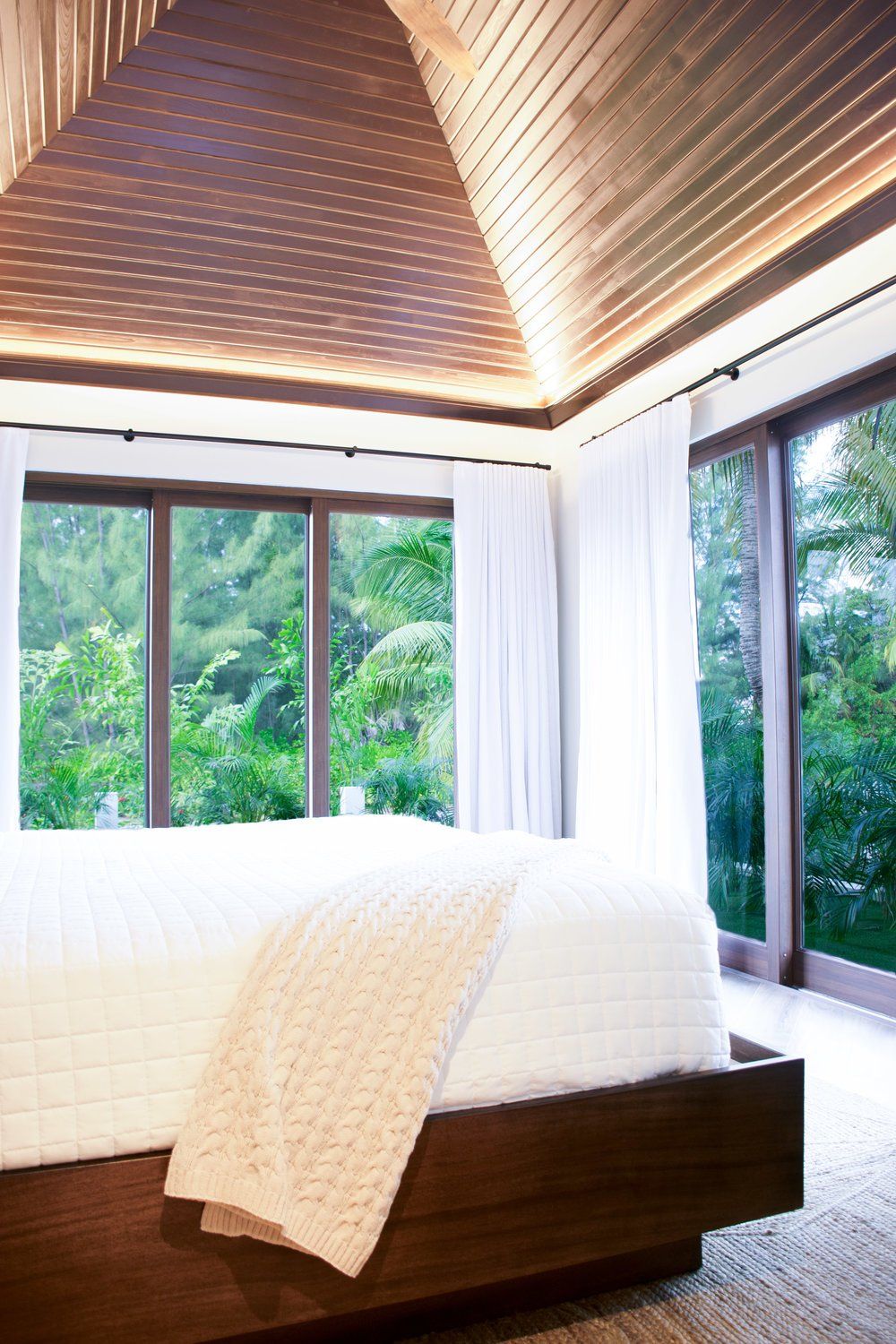 a bedroom with a large bed, lots of windows and a wooden ceiling .