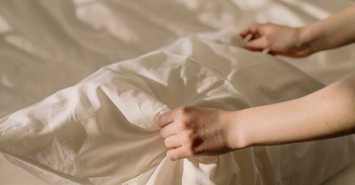 A person is making a bed with white sheets.