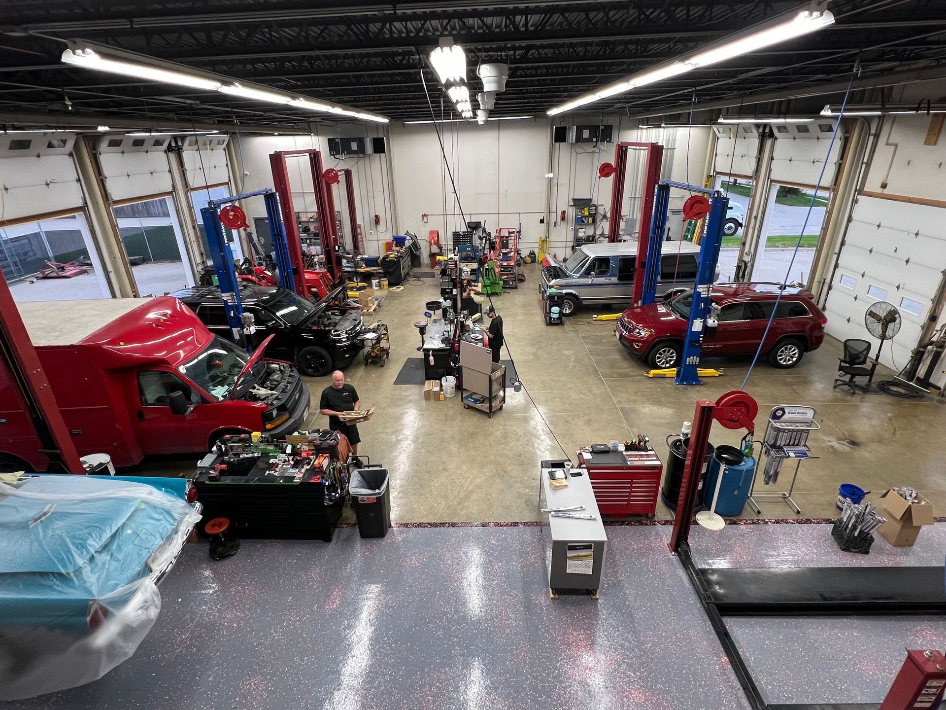 Inside a busy auto repair shop: cars on lifts, mechanics working.