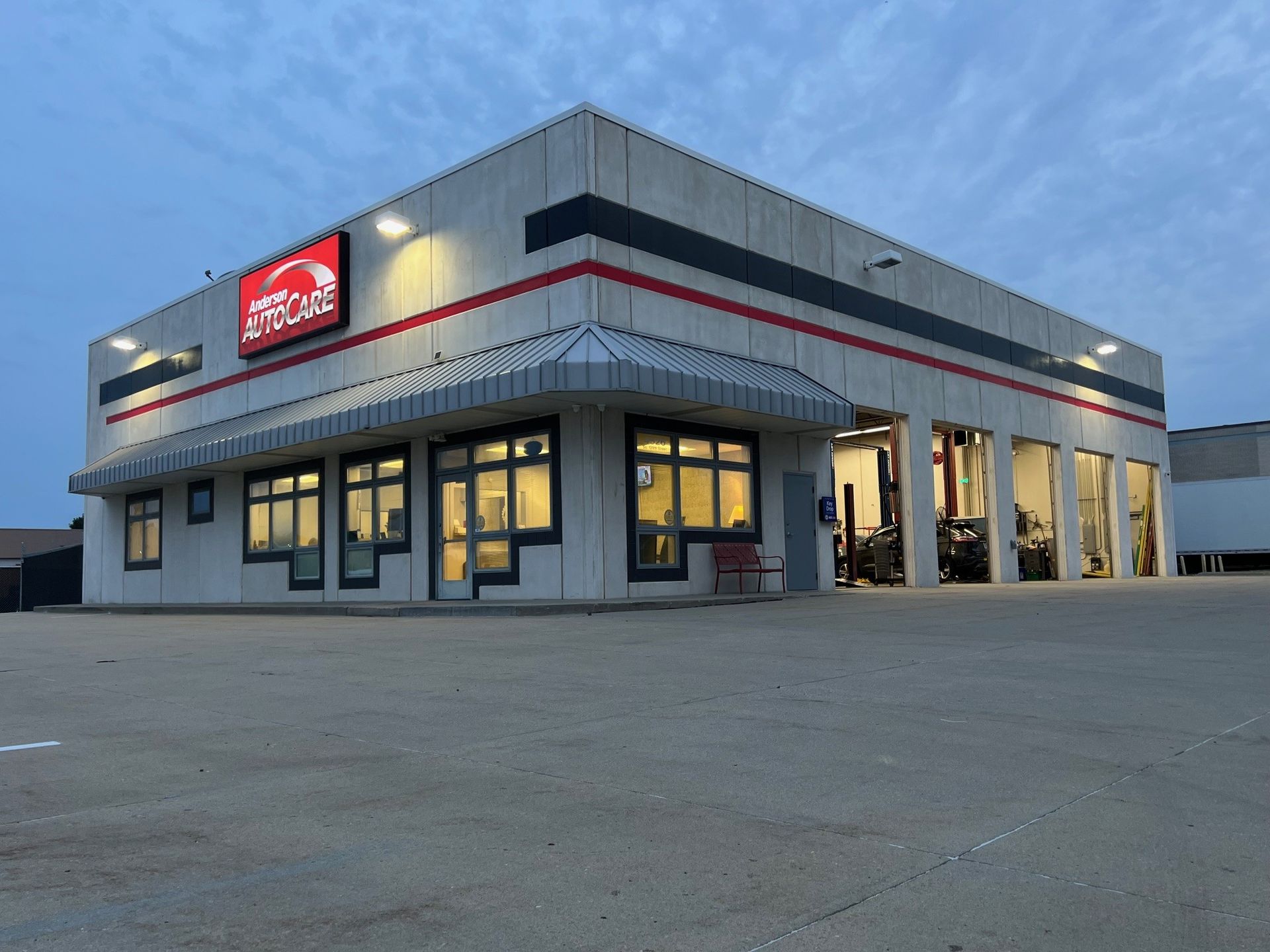 Auto repair shop exterior at dusk with illuminated sign and open bays.