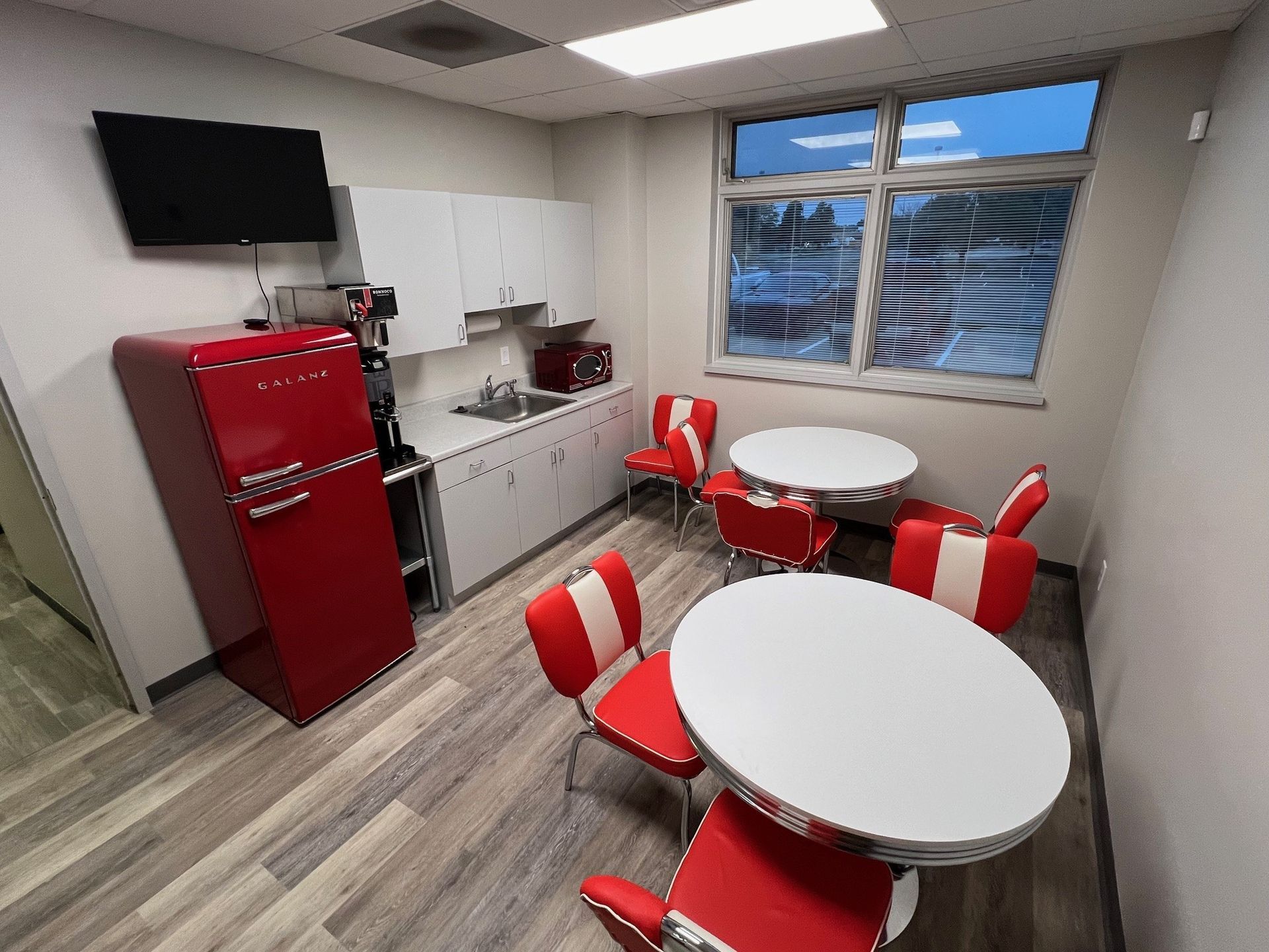 Retro kitchen with red refrigerator, white cabinets, tables, chairs, and window.