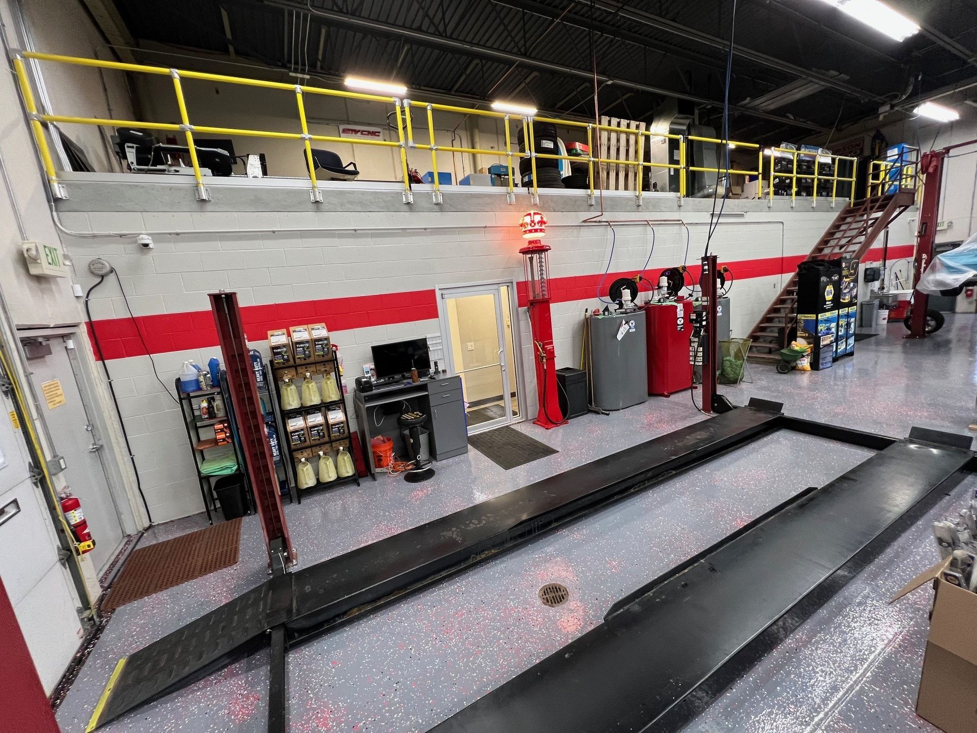 Interior of a car repair shop with a lift.  Mezzanine above.  Red and gray accents.