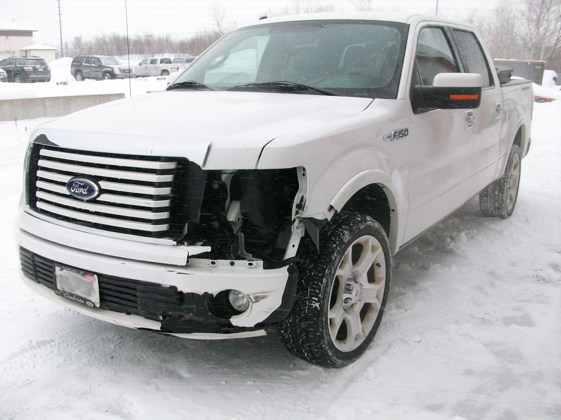 A white ford truck with a damaged front end is parked in the snow