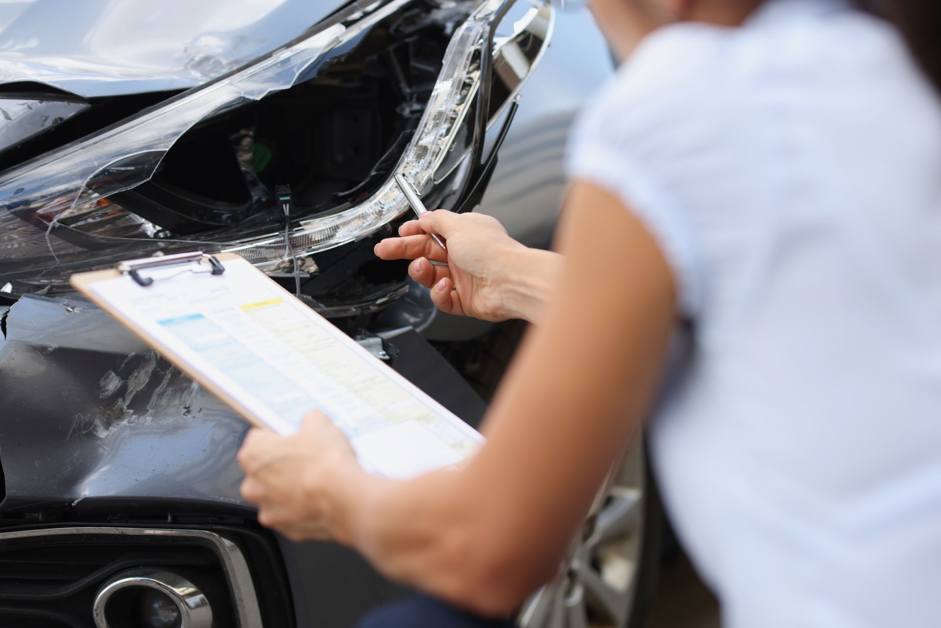 Person filling out an insurance form beside a damaged car after a collision