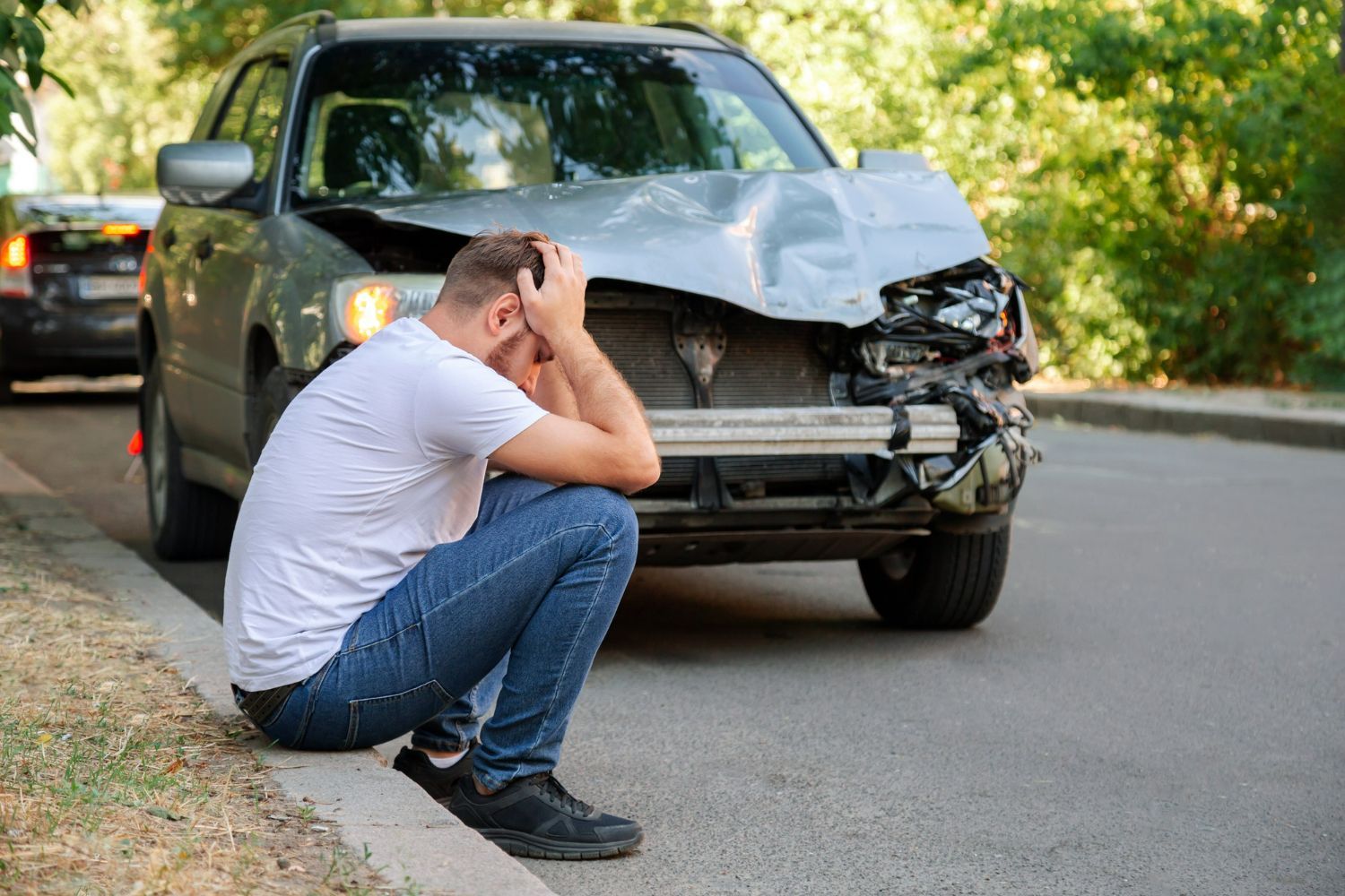 A man is kneeling down in front of a damaged car.