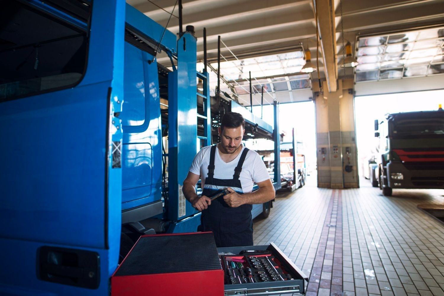 Mechanic in blue overalls working on a truck in a garage, selecting a tool from a tray.
