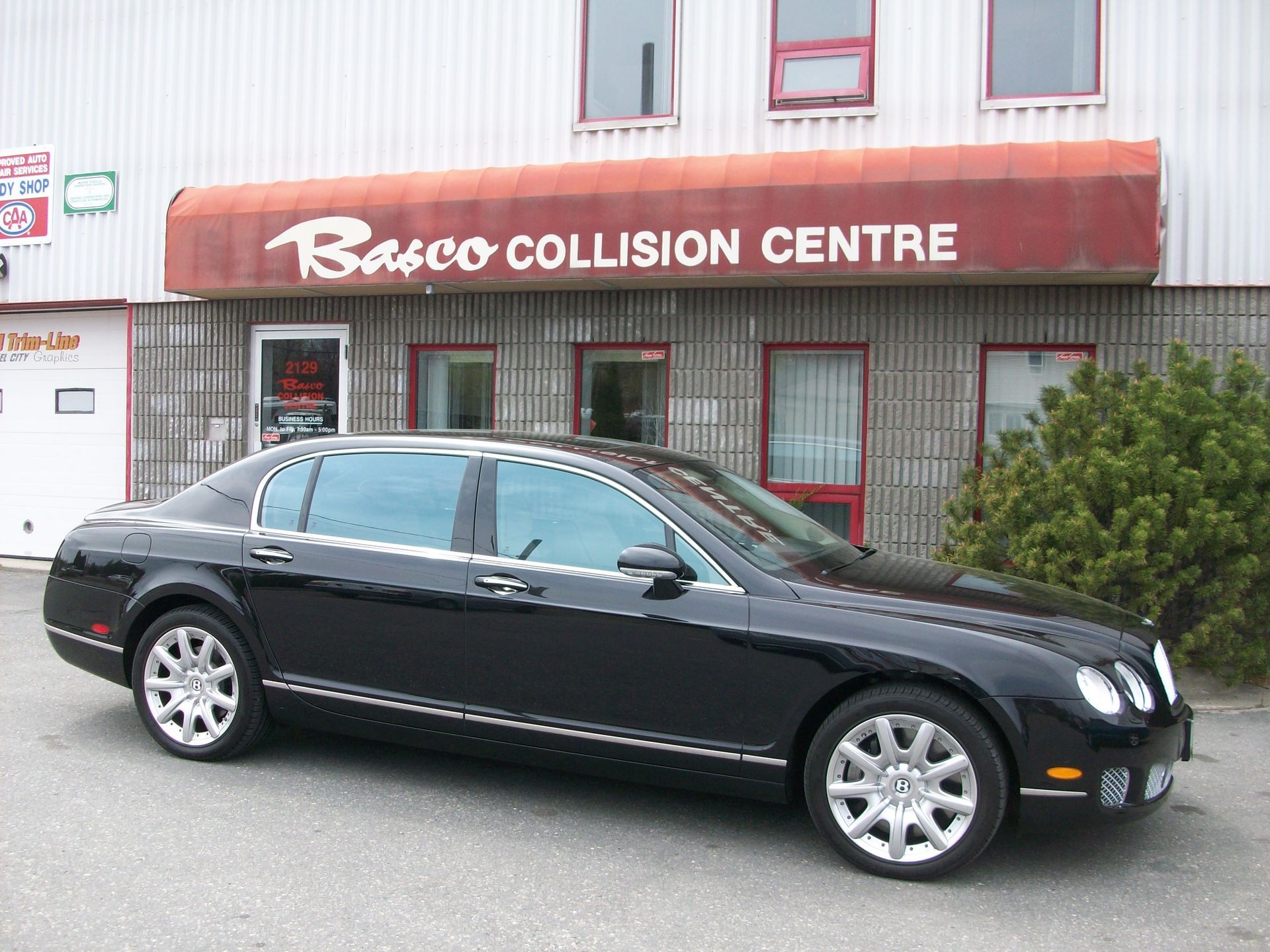 Black Bentley sedan parked in front of Basco Collision Centre with red awning.
