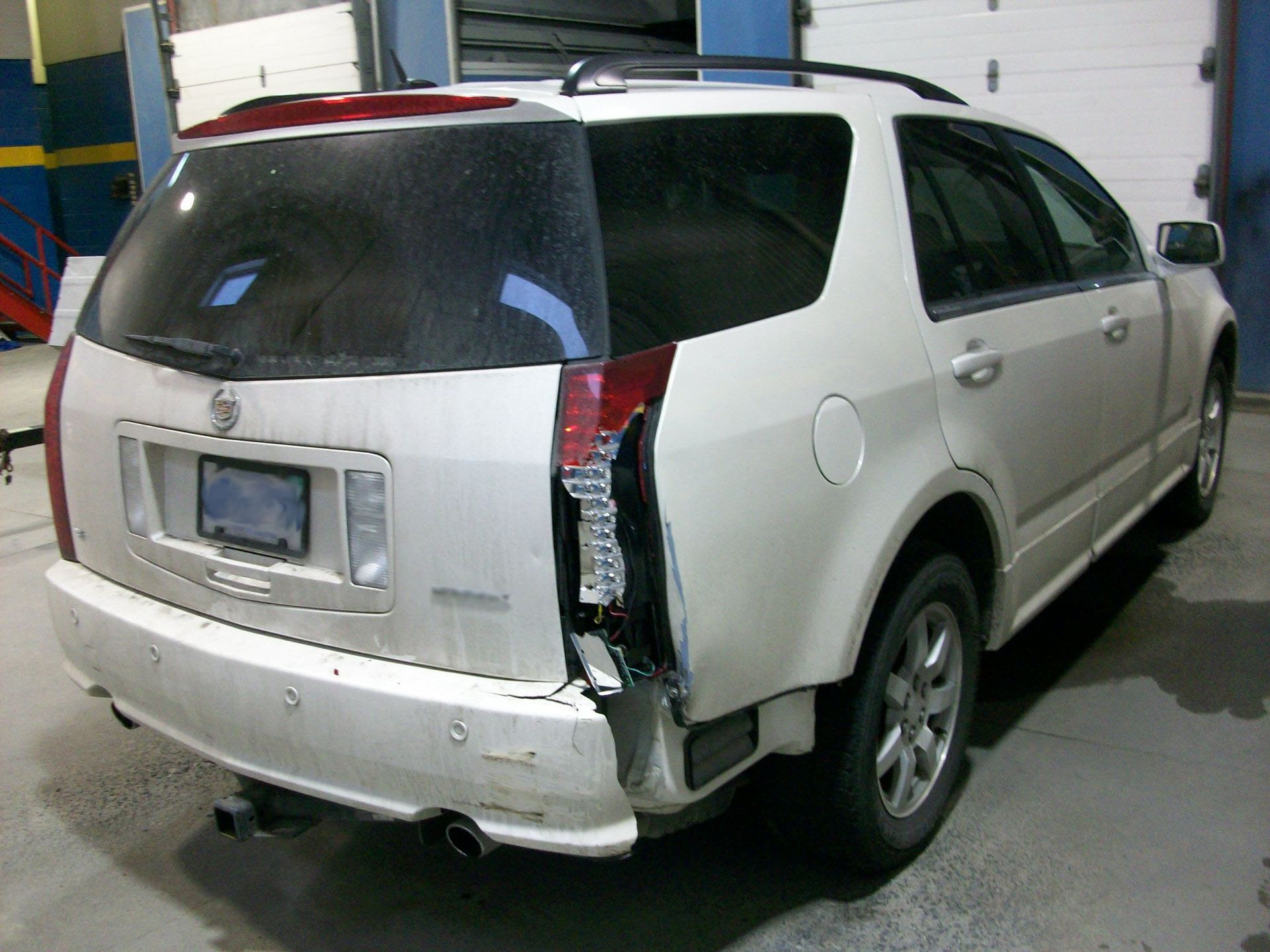 A white car with a broken tail light is parked in a garage