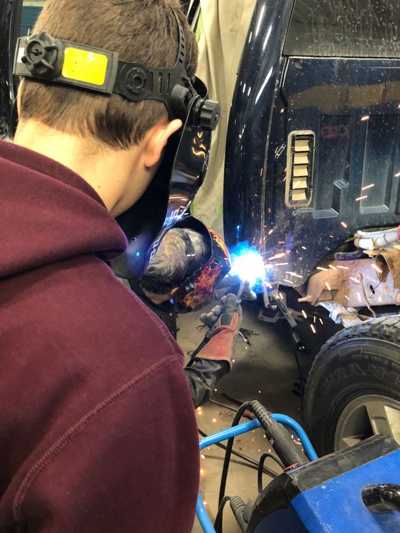 A man wearing a welding mask is welding a car