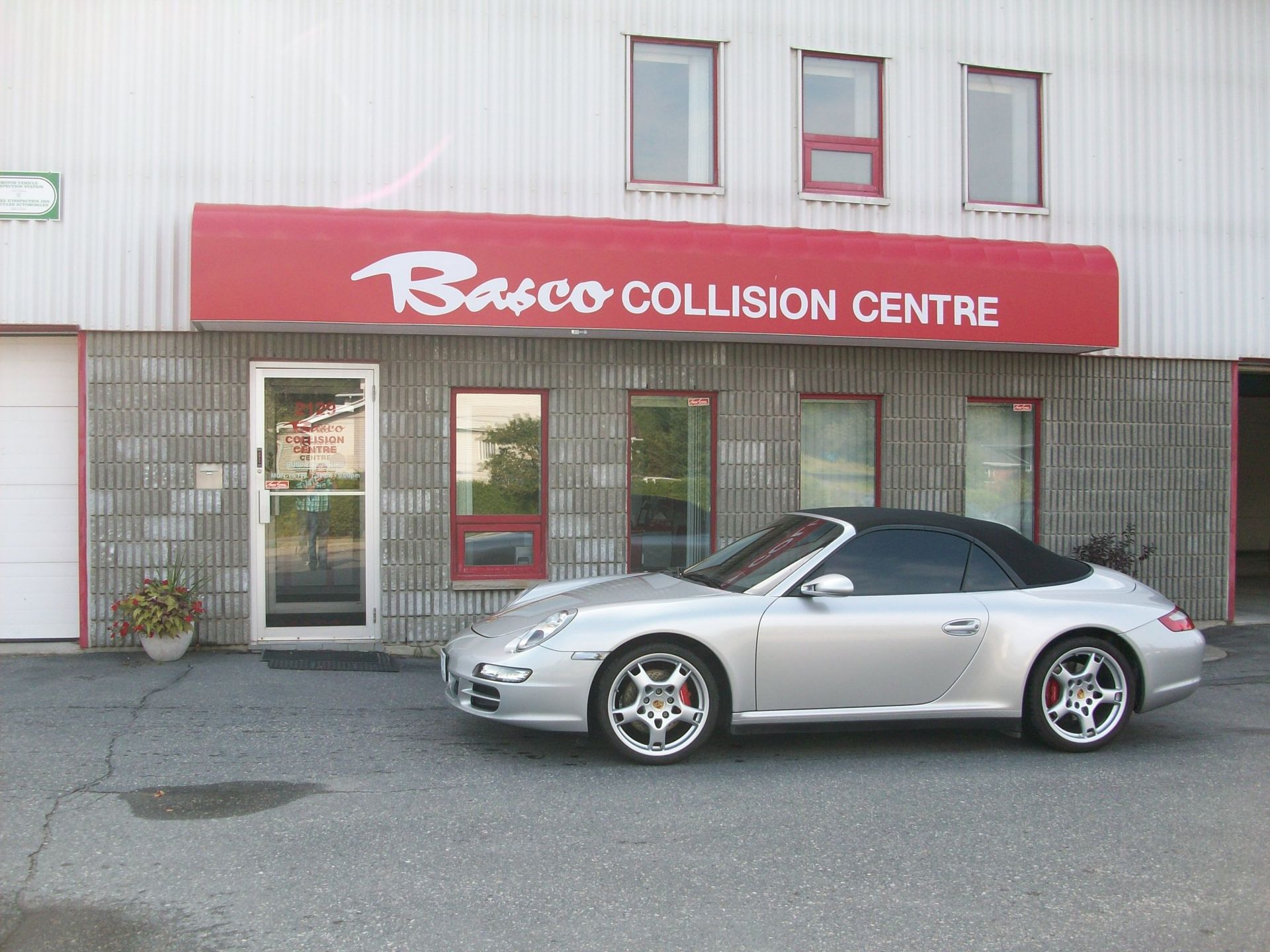 A silver car is parked in front of a building that says barco collision centre