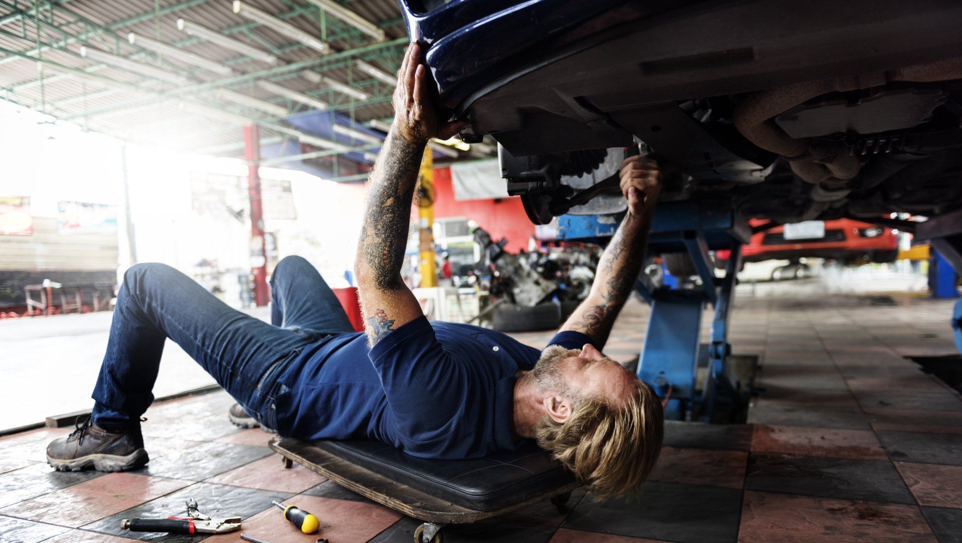 A man is laying on a skateboard under a car in a garage.