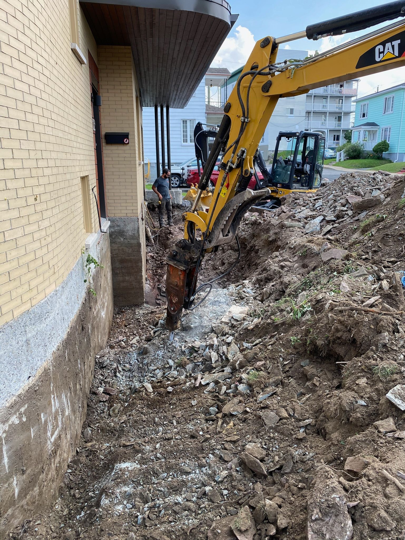 Une grande excavatrice jaune creuse un trou devant un bâtiment.