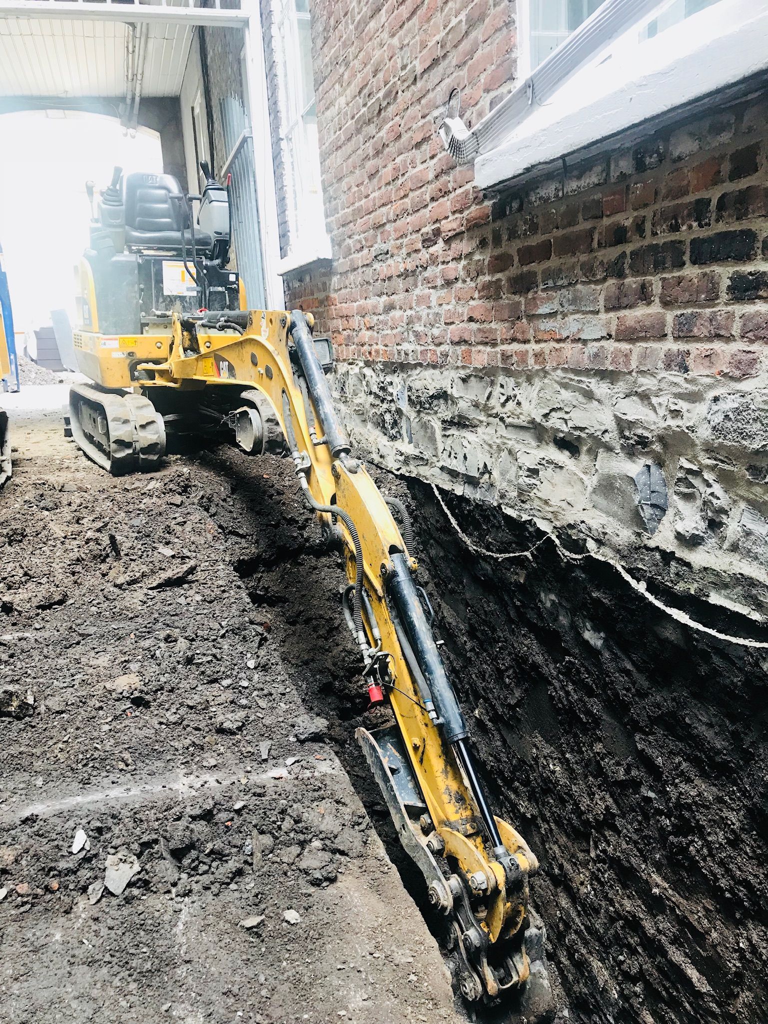 Une excavatrice jaune creuse un trou devant un bâtiment en briques.