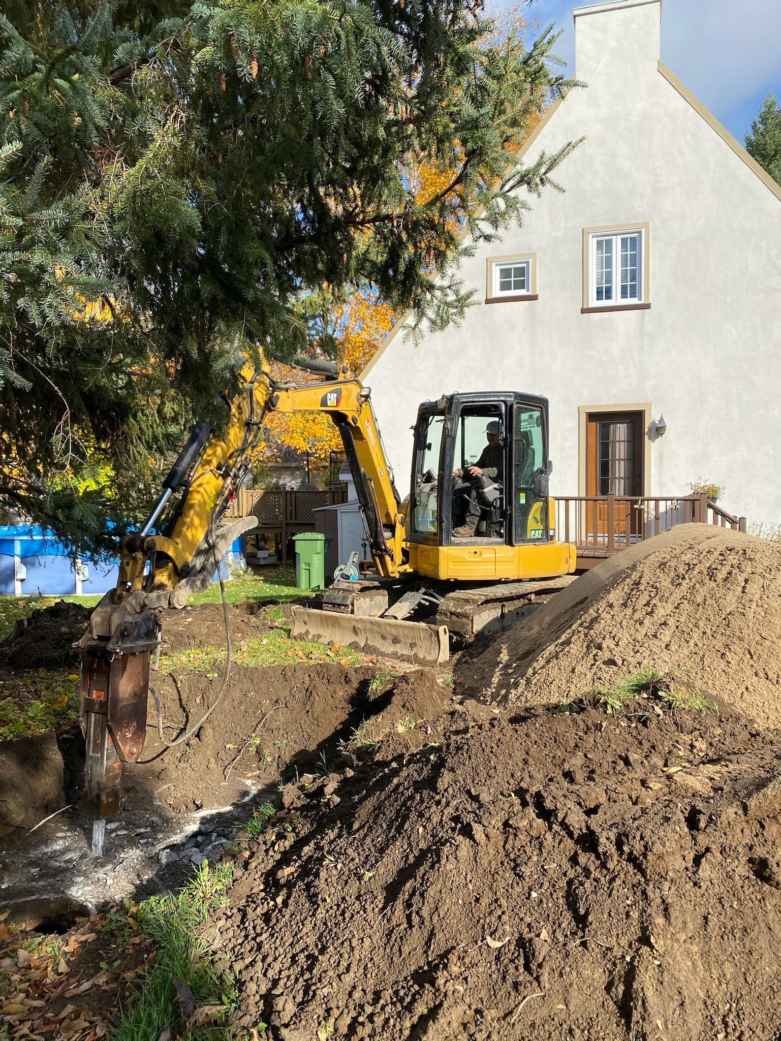 Une excavatrice jaune creuse un trou devant une maison blanche.