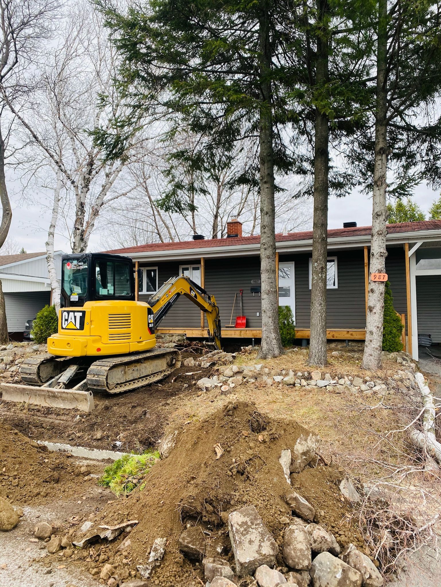 Une excavatrice jaune creuse un trou devant une maison.