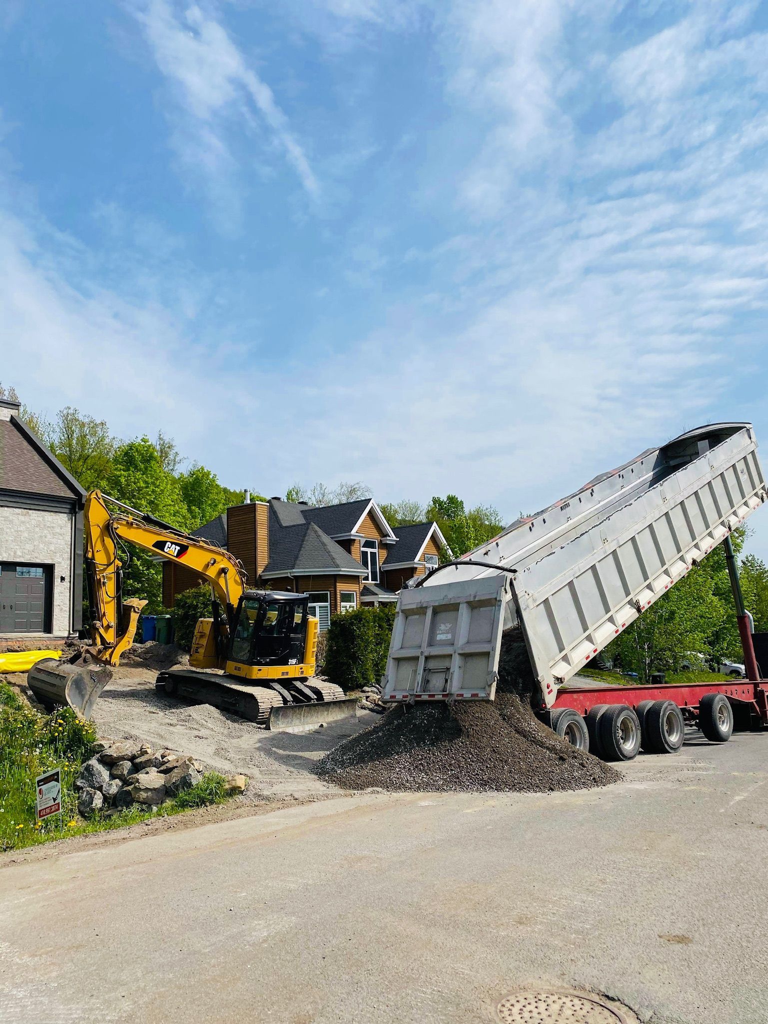 Un camion à benne basculante est en train d'être chargé de terre devant une maison.