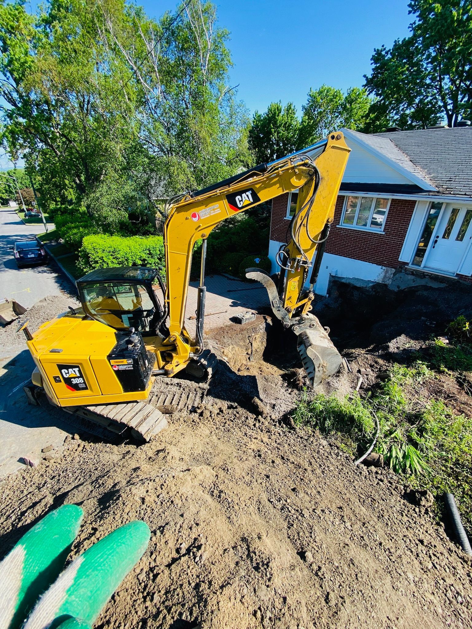 Une excavatrice jaune creuse un trou devant une maison.