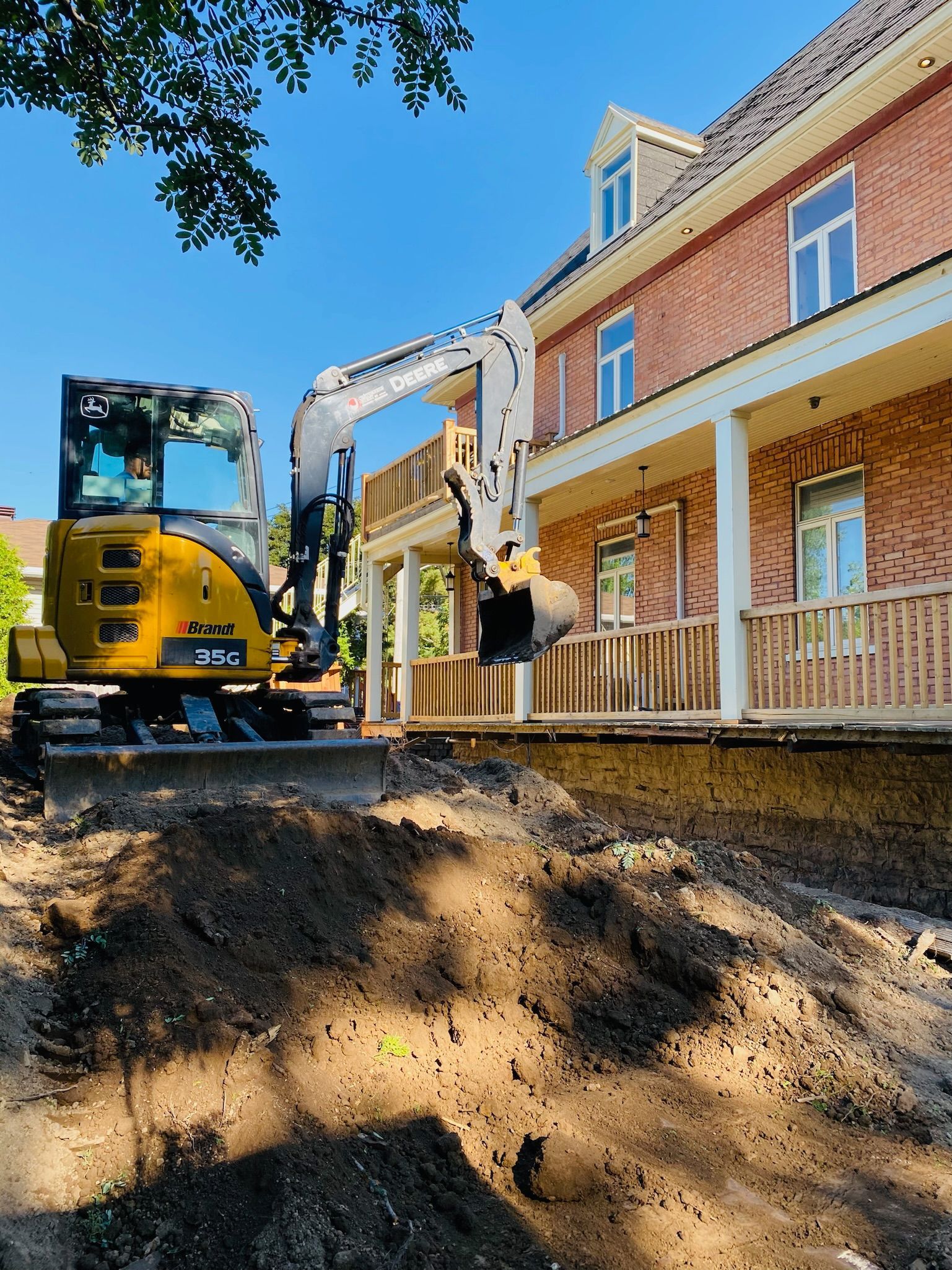 Une excavatrice jaune creuse un trou devant une maison en briques.