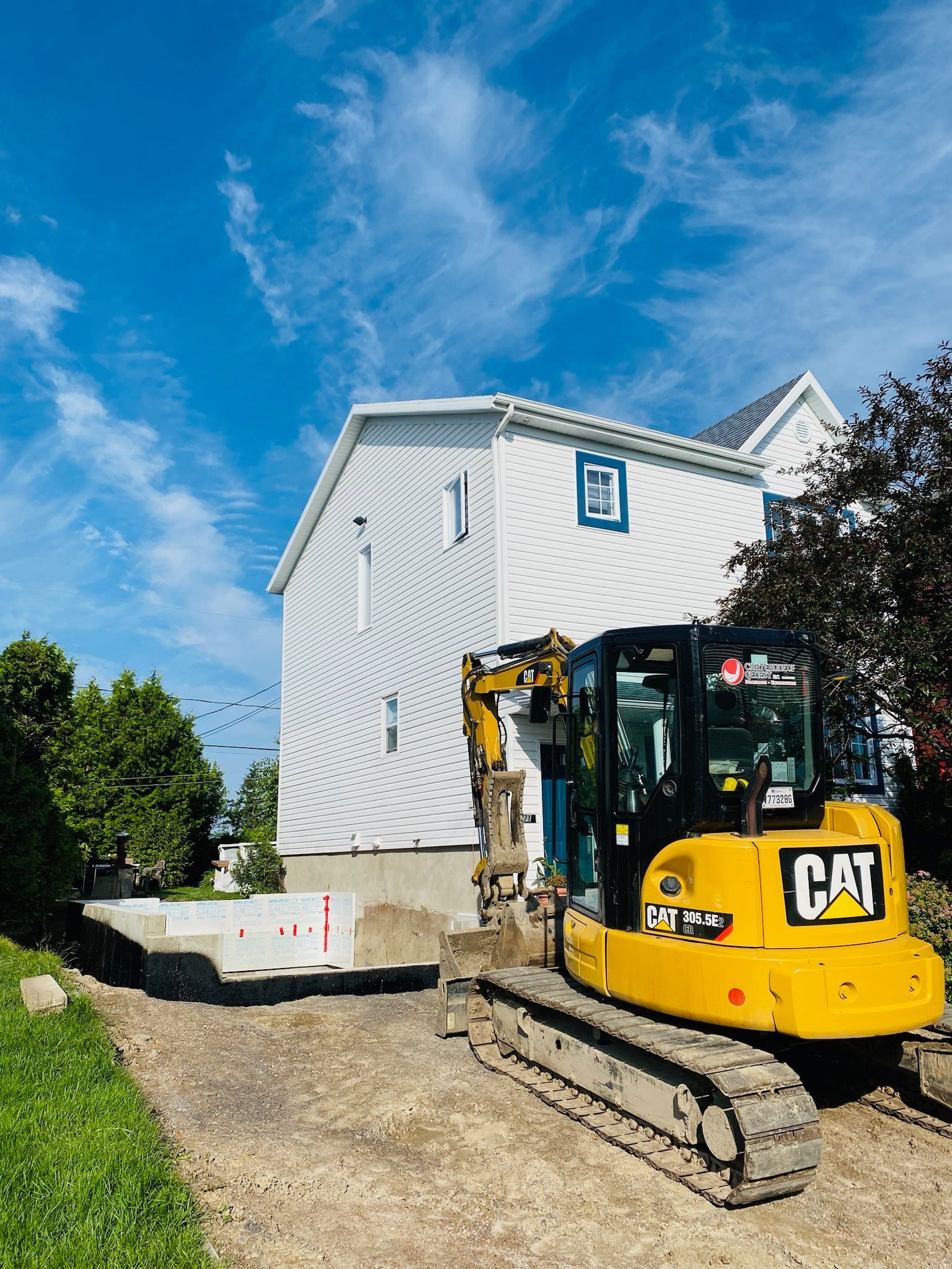 Une excavatrice jaune est garée devant une maison blanche.