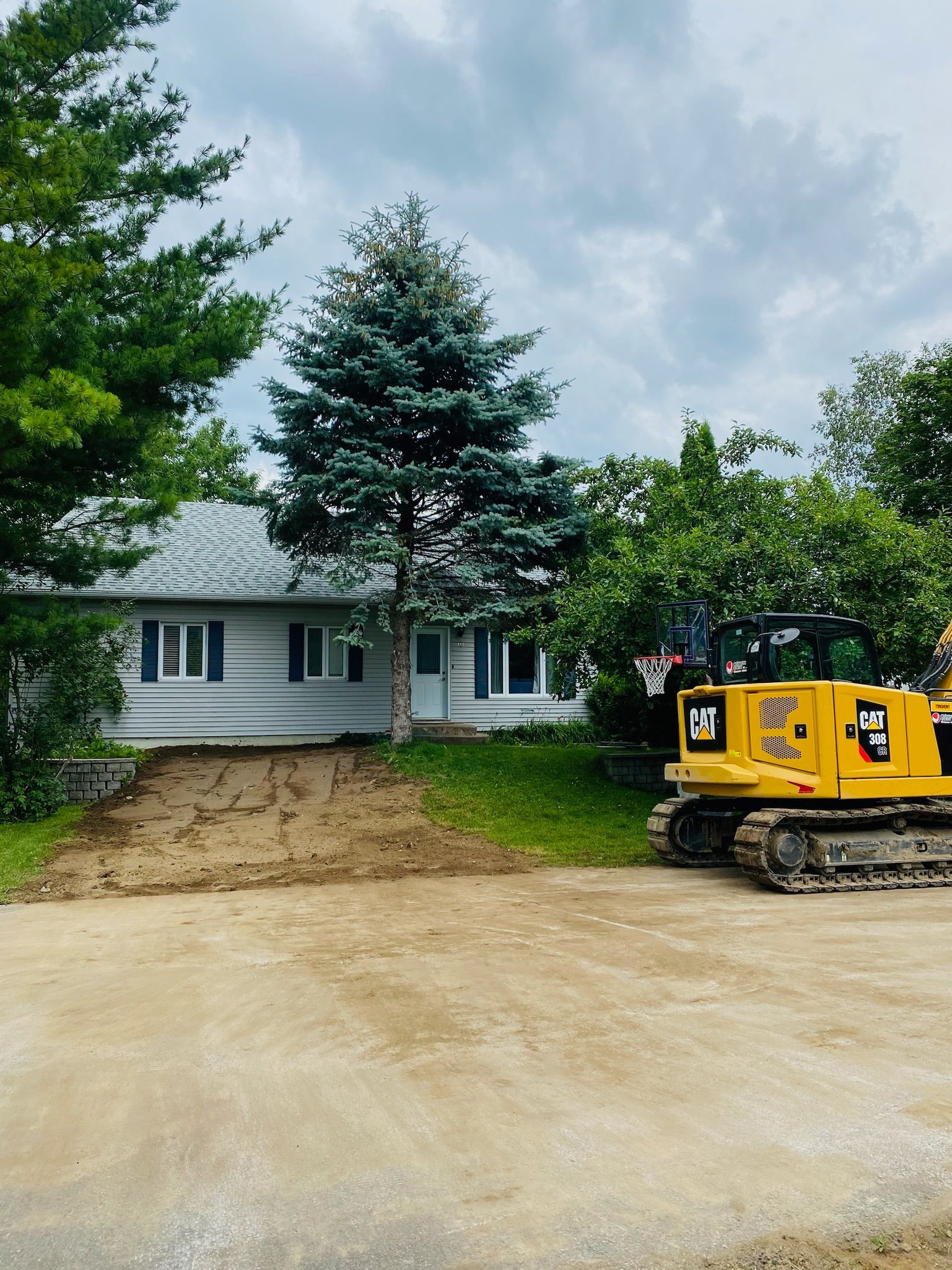 Une excavatrice jaune est garée devant une maison.