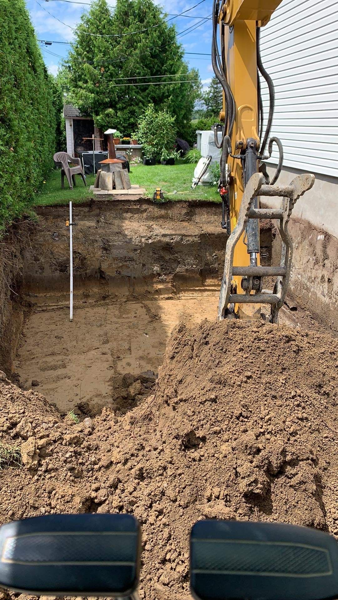 Une excavatrice creuse un trou dans le sol devant une maison.