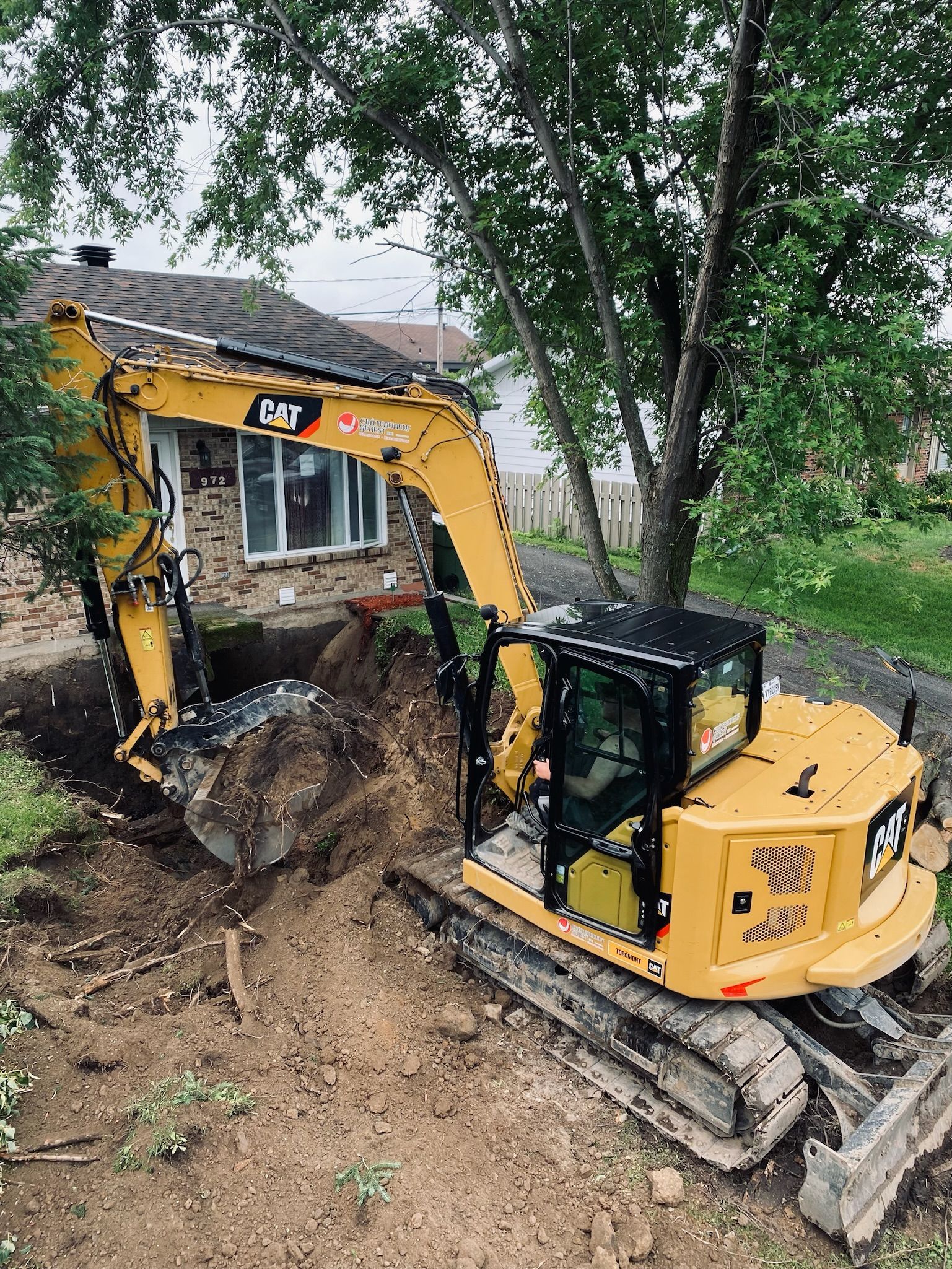 Une excavatrice jaune creuse un trou devant une maison.