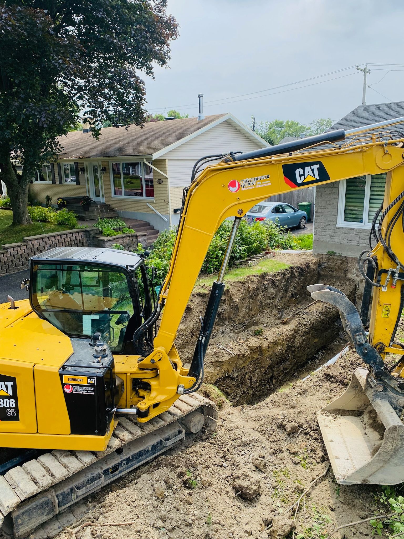 Une excavatrice jaune creuse un trou dans la terre devant une maison.