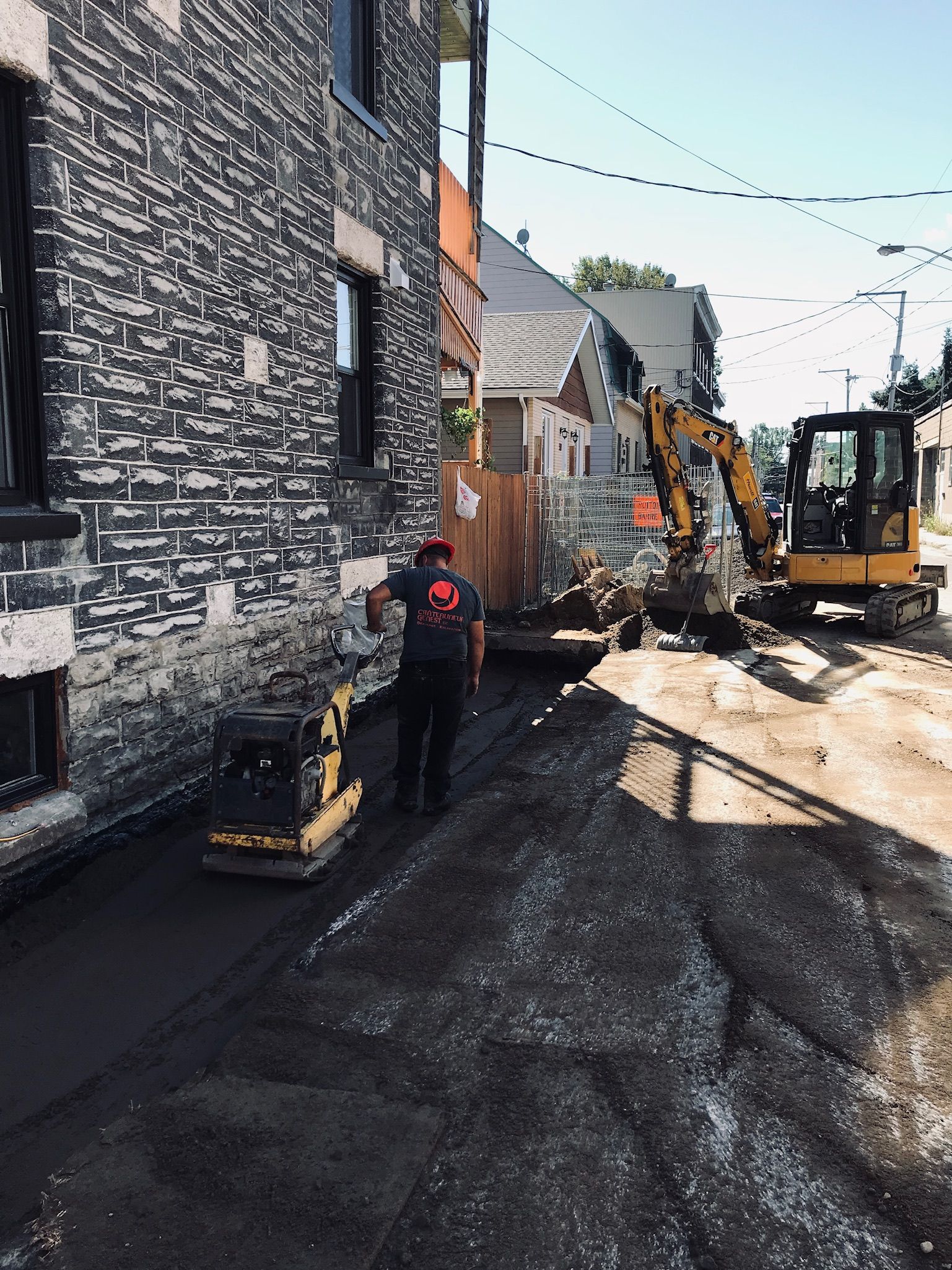 Un homme marche sur un chemin de terre devant un bâtiment en briques.