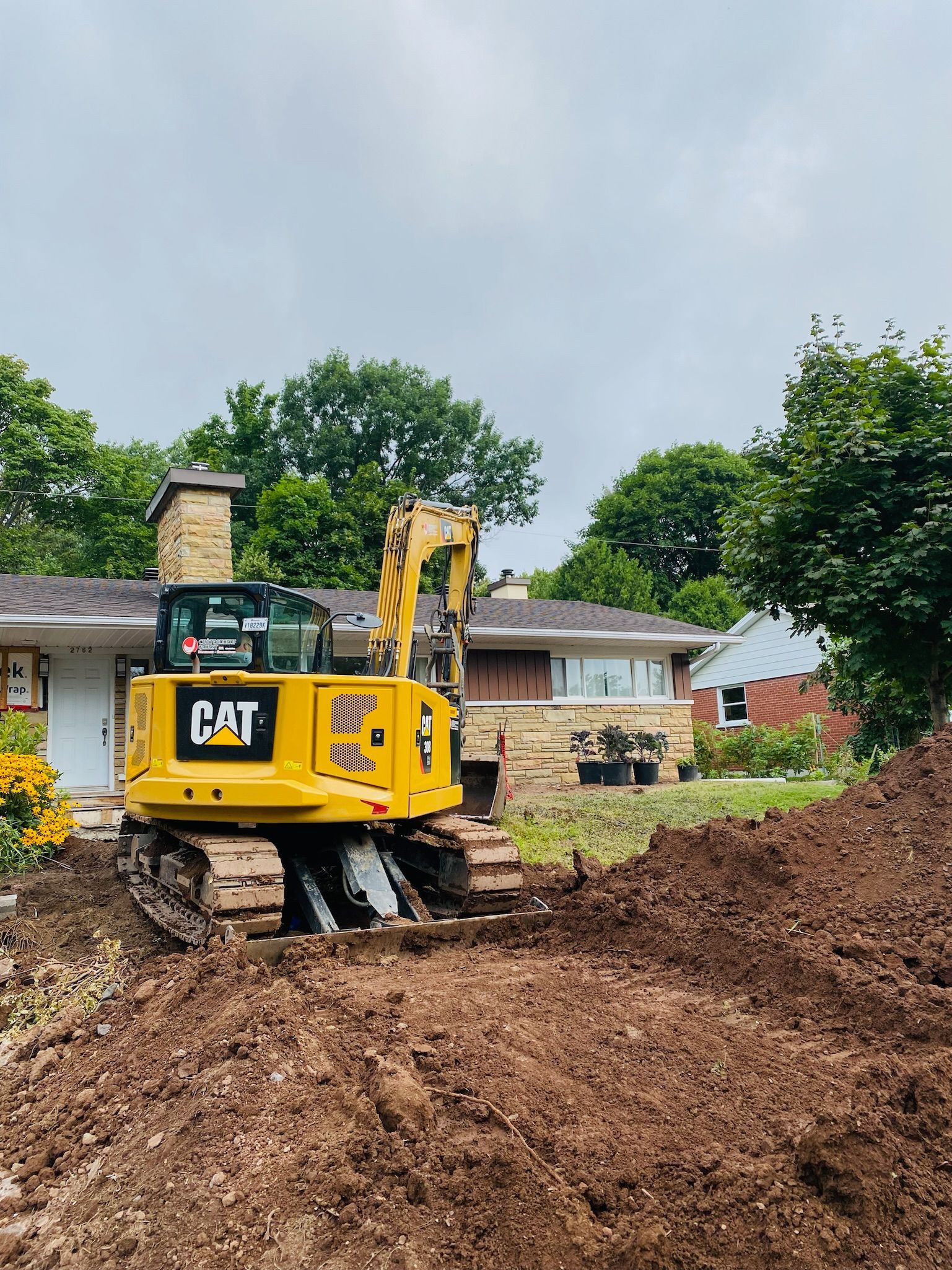 Une excavatrice jaune déplace de la terre devant une maison.