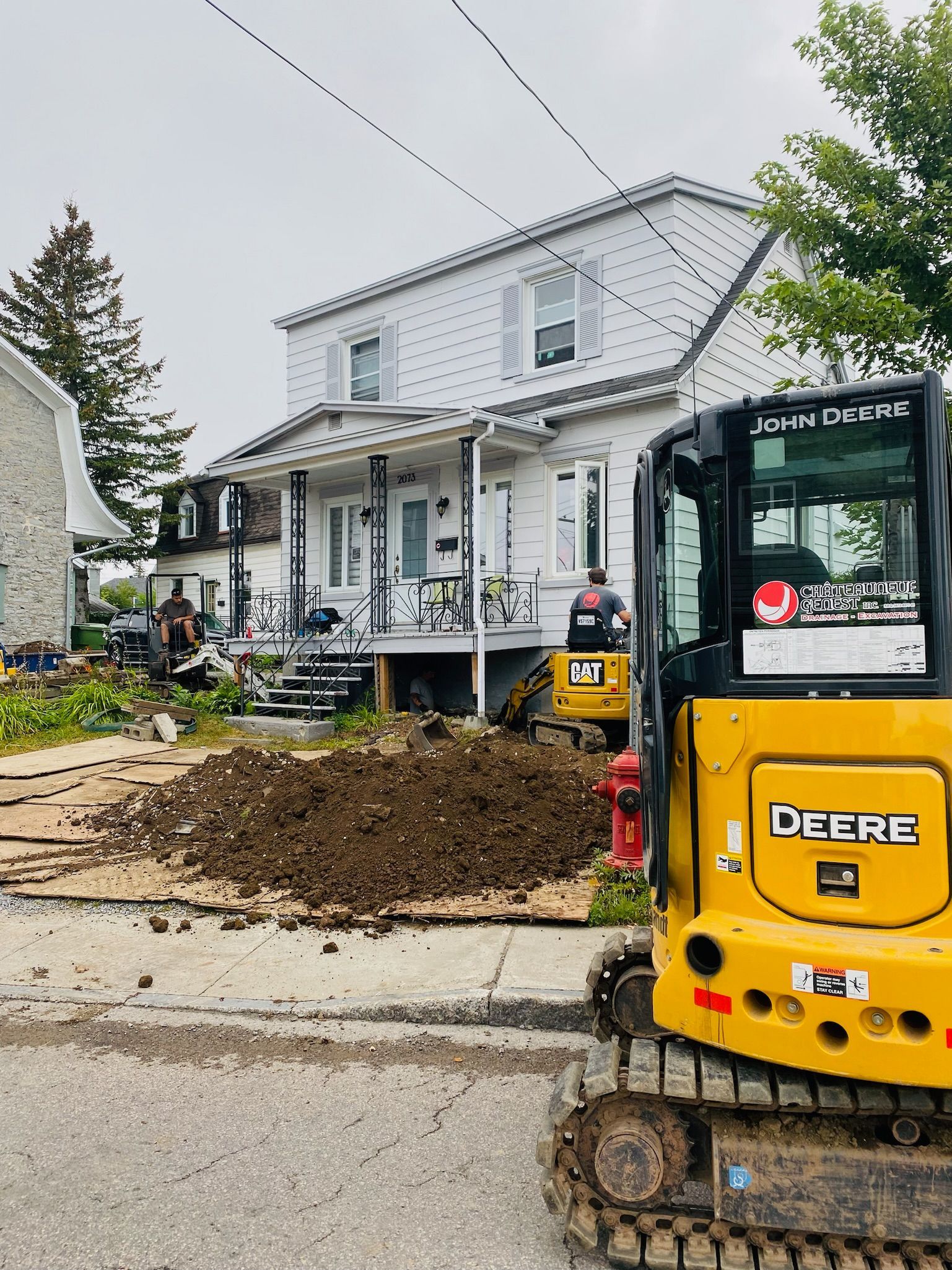 Une excavatrice Yellow Deere est garée devant une maison.