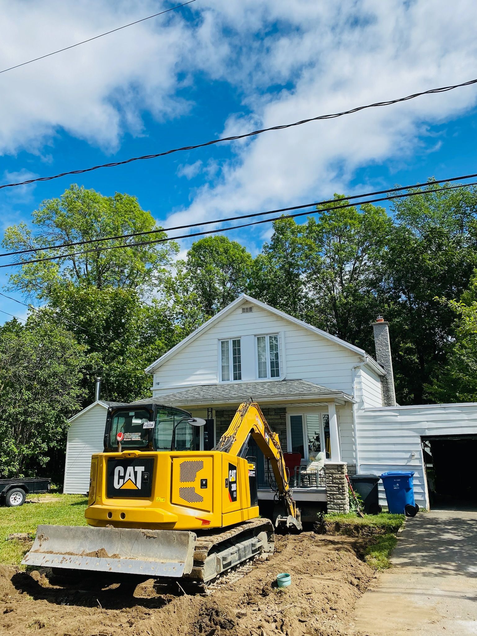 Une excavatrice jaune est garée devant une maison blanche
