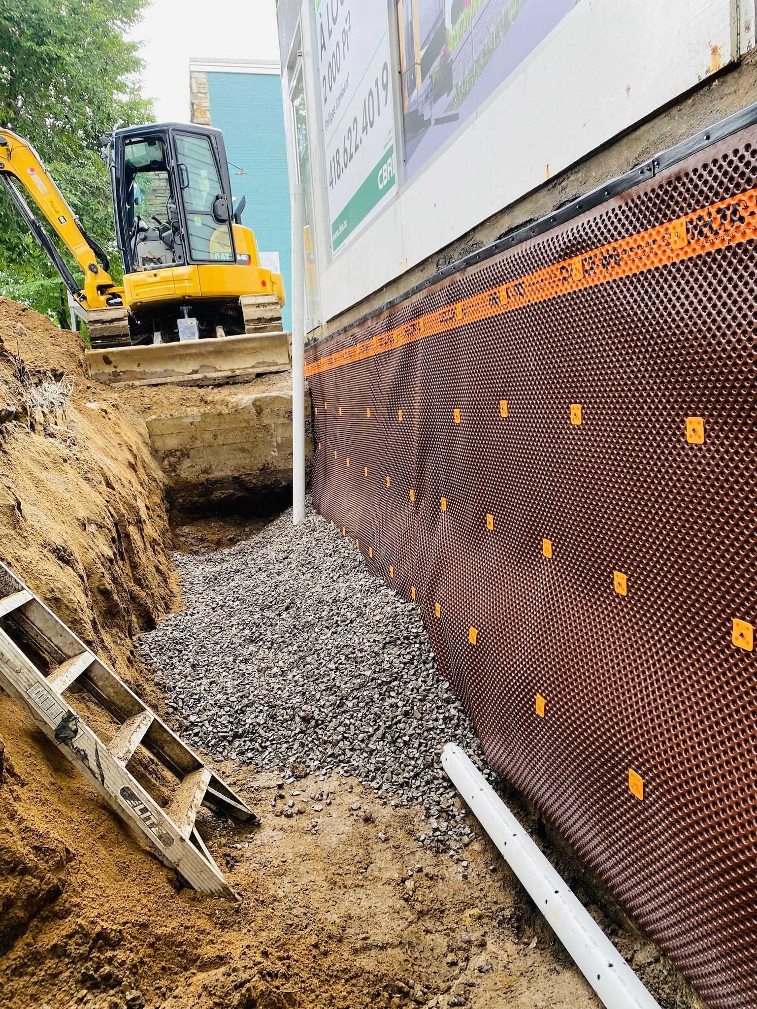 Une excavatrice jaune creuse un trou dans le sol à côté d'un bâtiment.