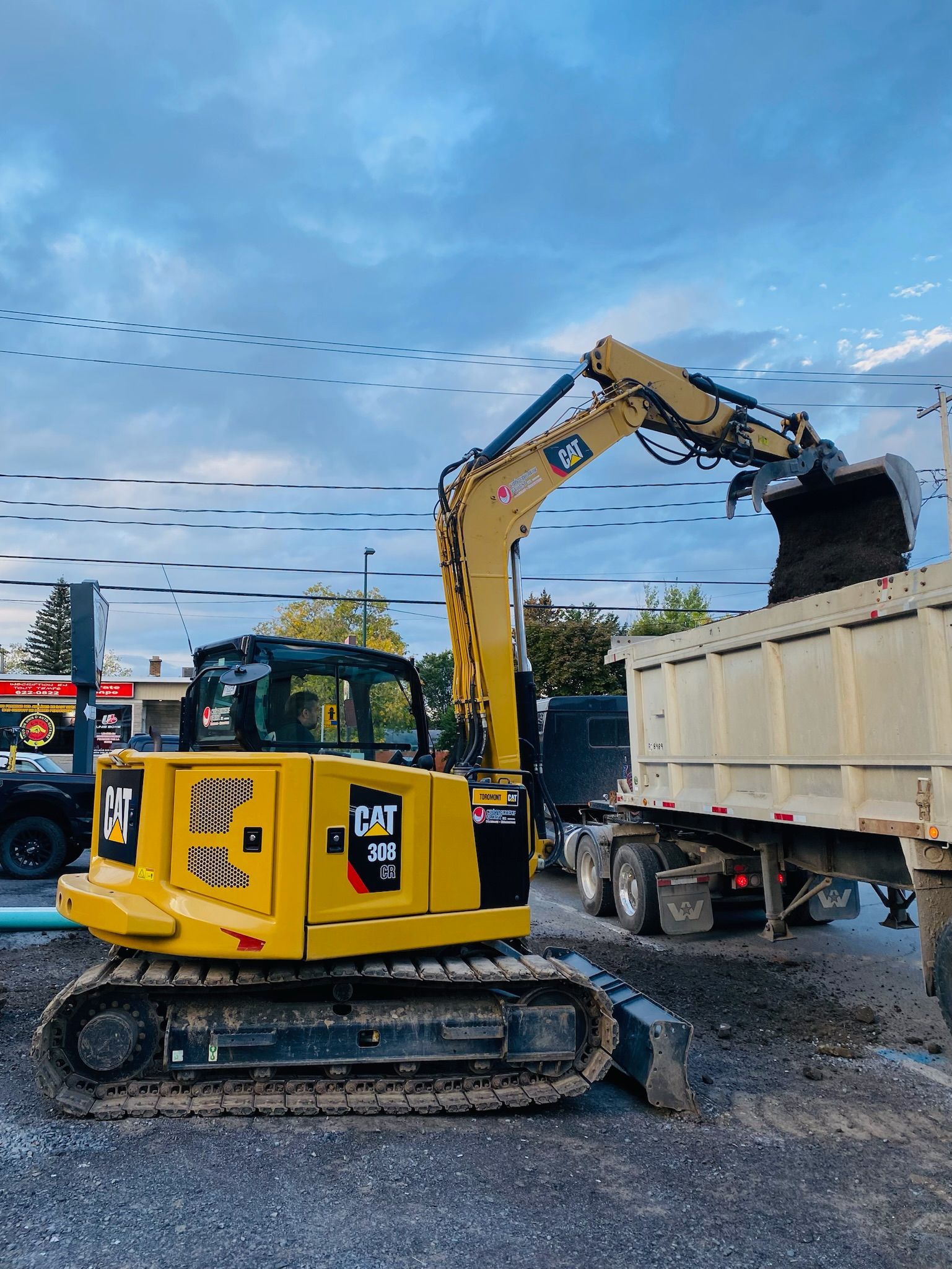 Une excavatrice jaune charge du gravier dans un camion à benne basculante.