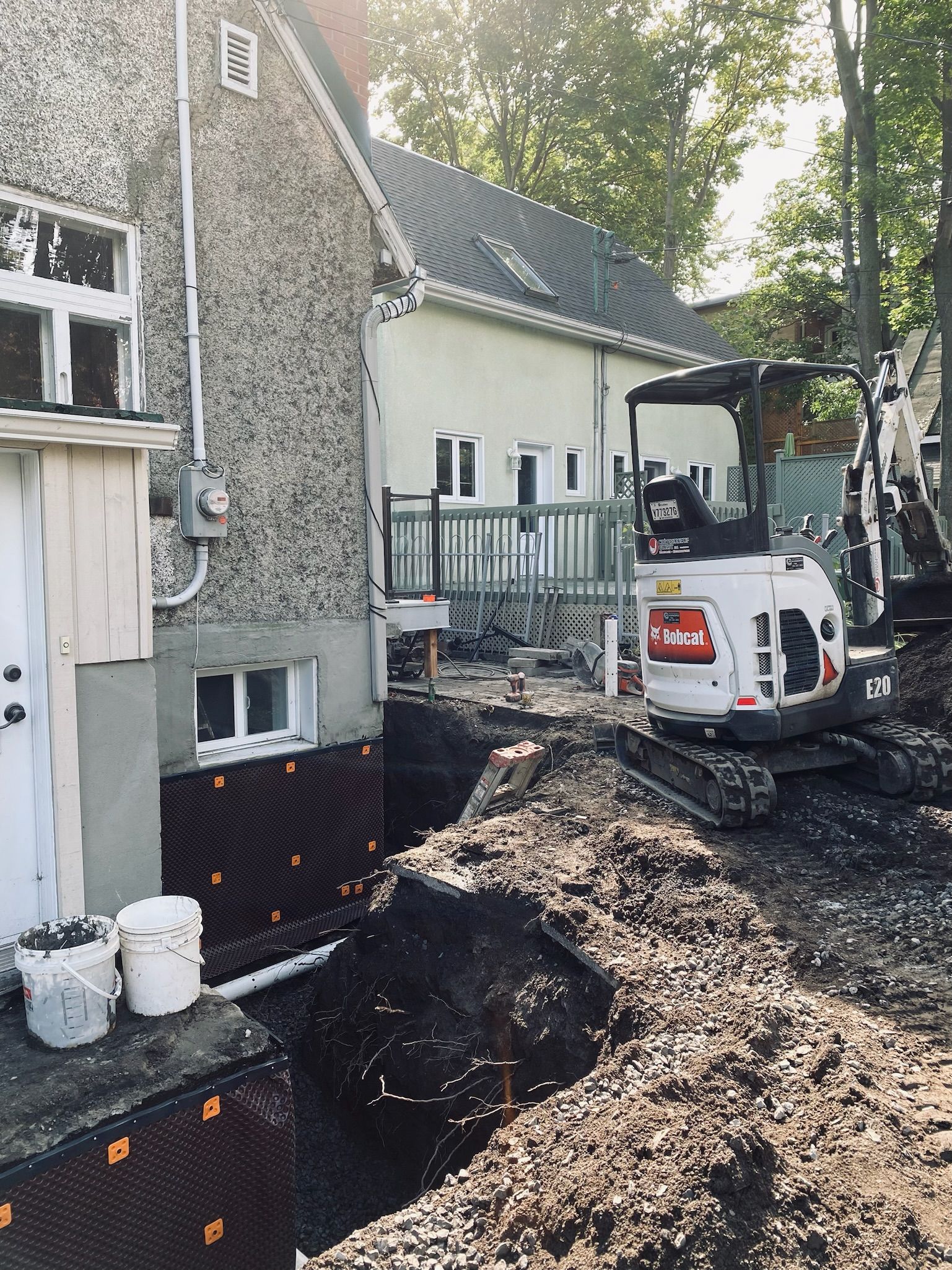 Une petite excavatrice creuse un trou devant une maison.