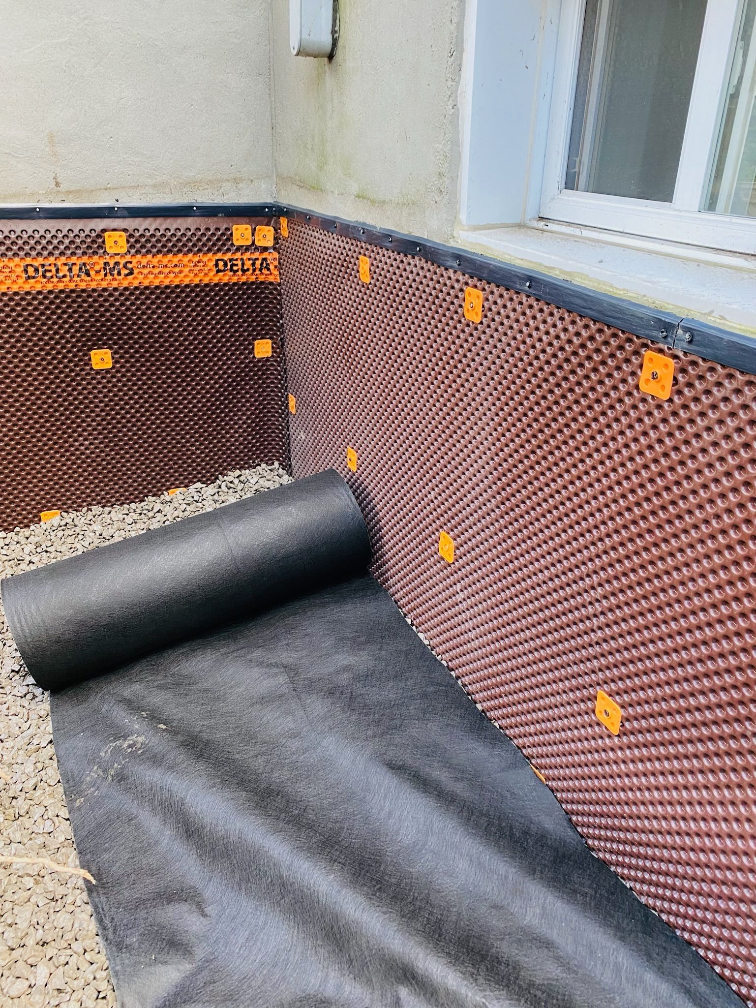 Un rouleau de membrane drainante est en cours d'installation sur le côté d'une maison.