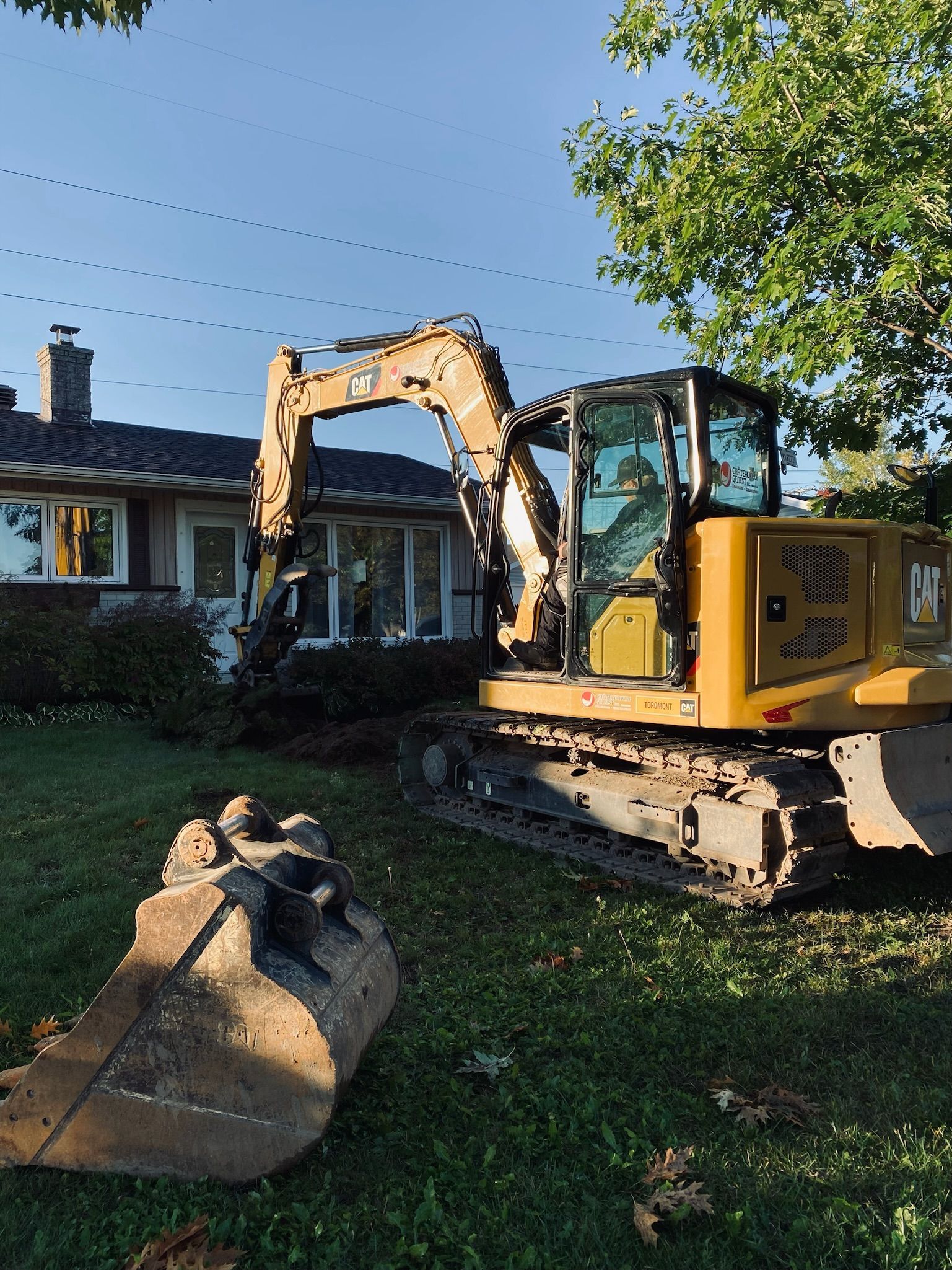 Une excavatrice jaune est assise devant une maison.