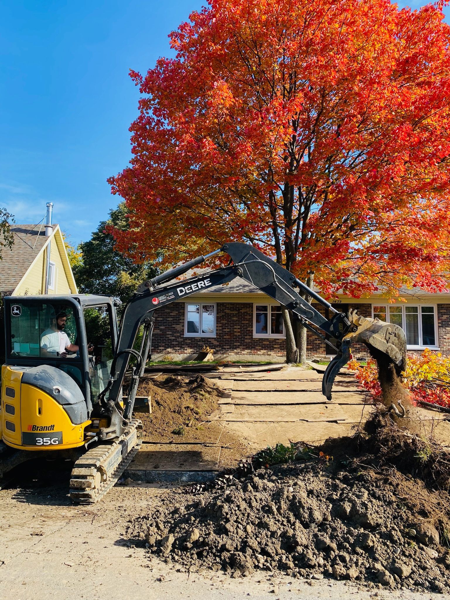 Une excavatrice jaune creuse un trou devant une maison.