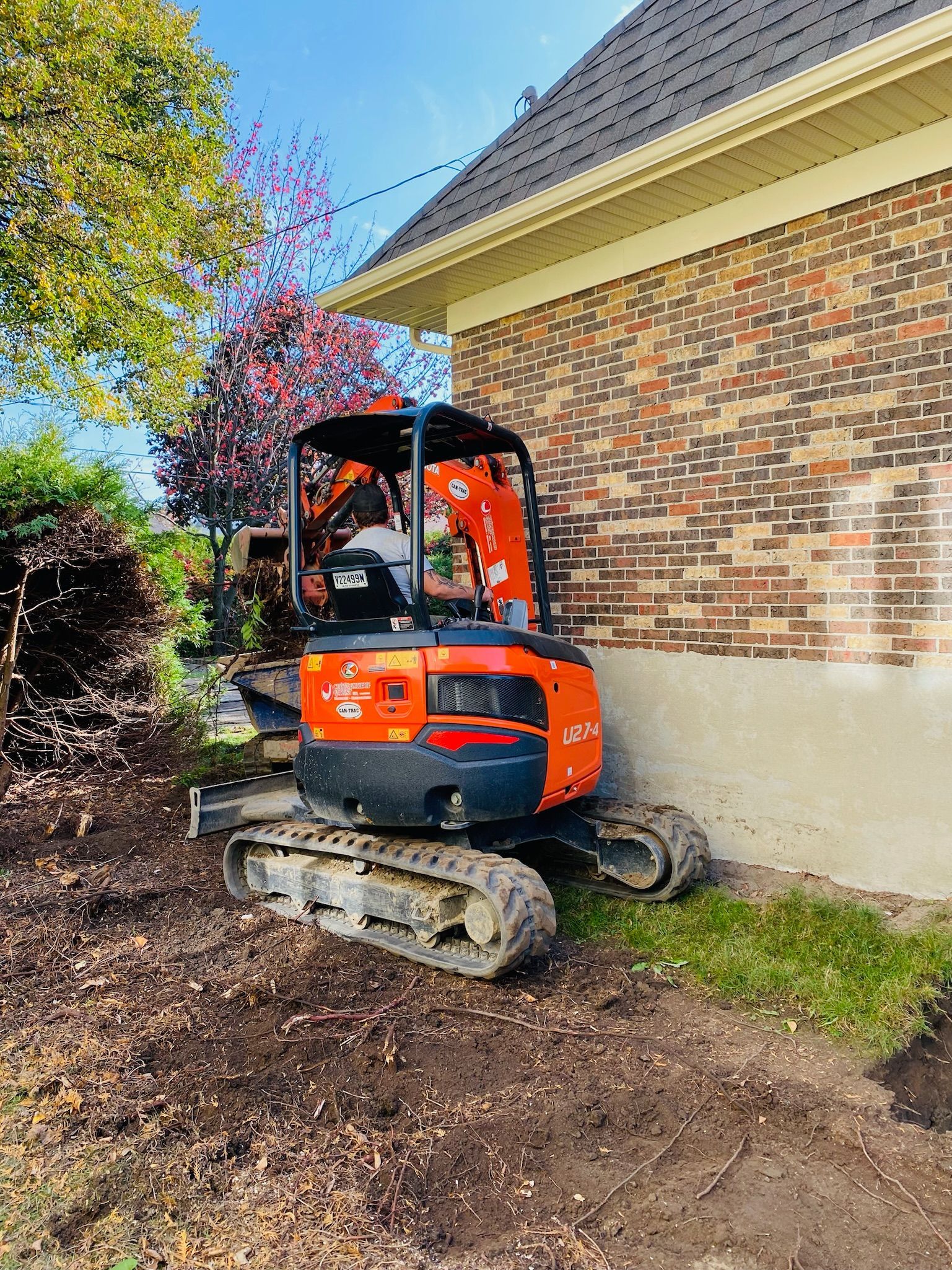 Une petite excavatrice orange et noire est garée devant une maison en briques.