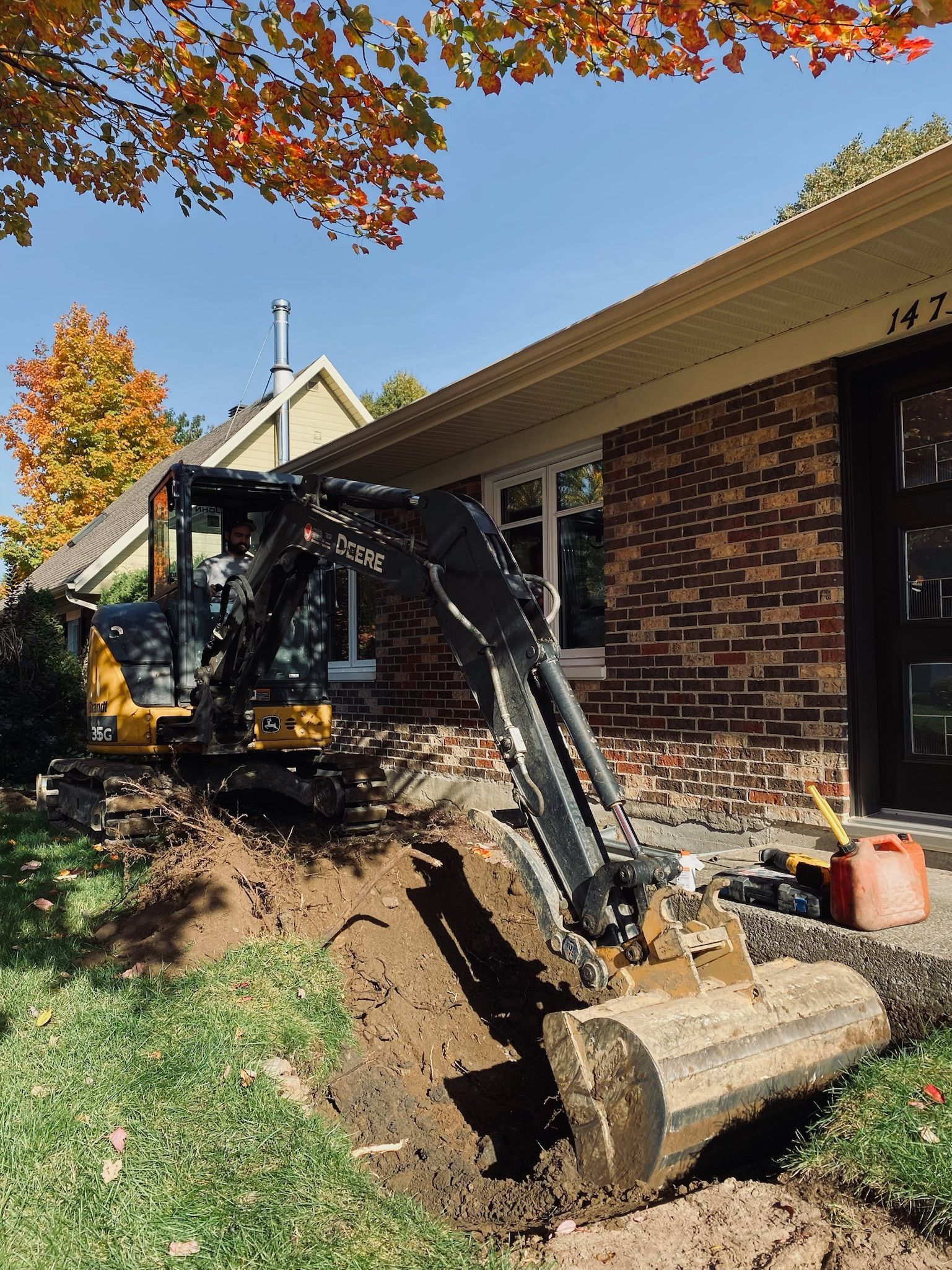 Une excavatrice creuse un trou devant une maison en briques.