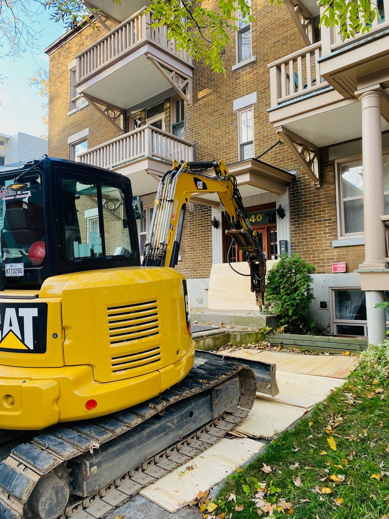 Une excavatrice jaune est garée devant un bâtiment en briques.