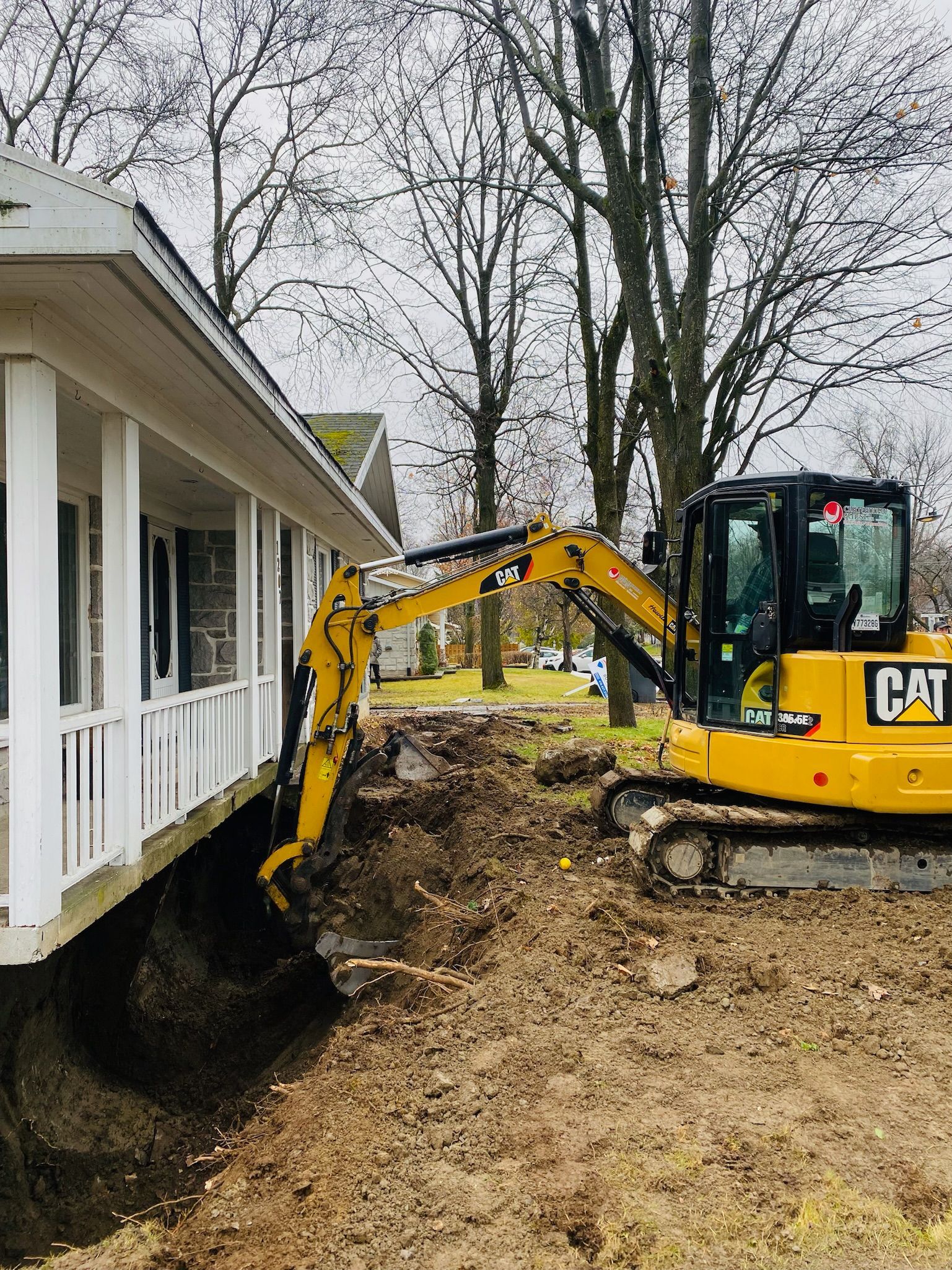 Une excavatrice jaune creuse un trou devant une maison.