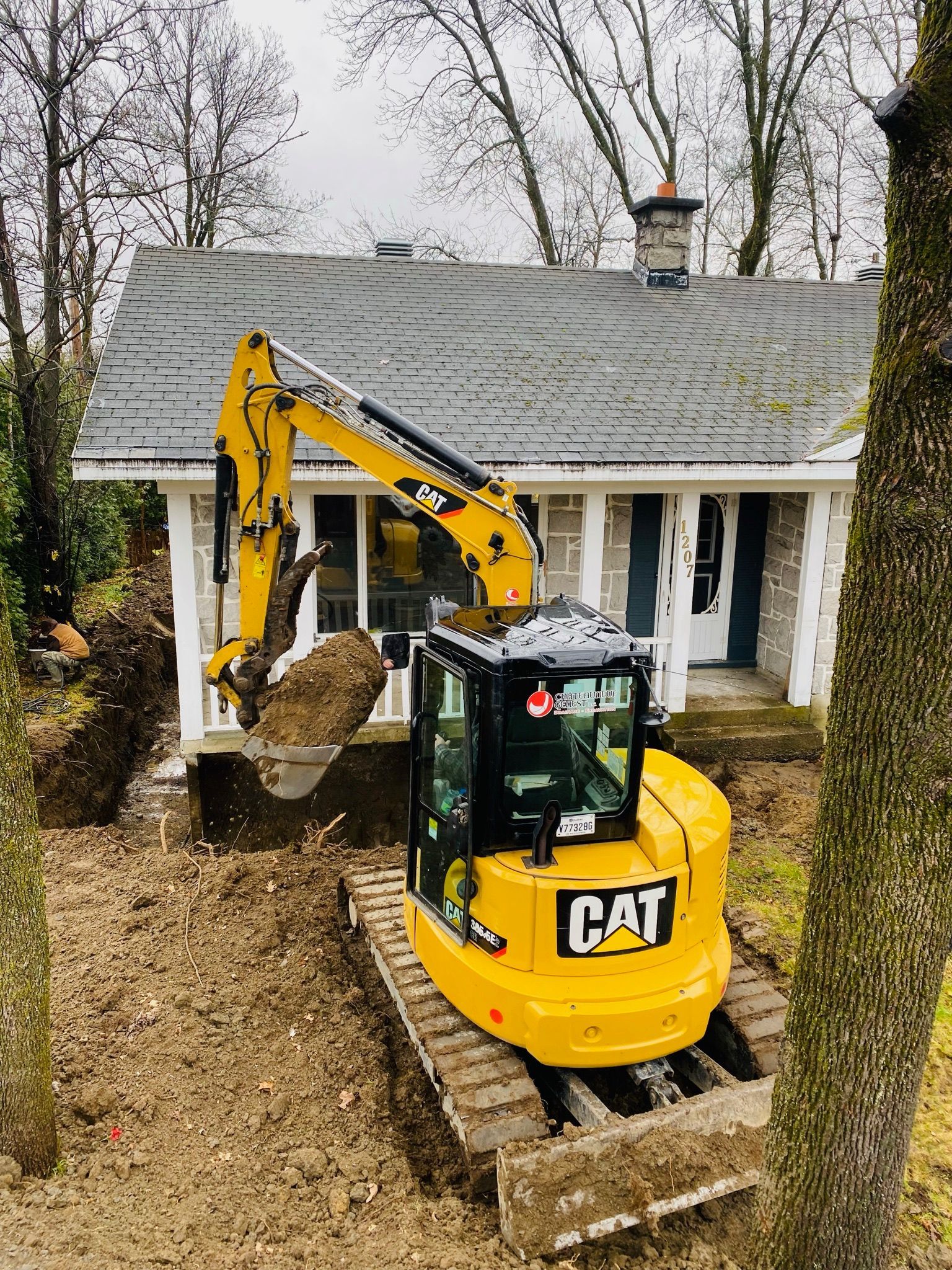 Une excavatrice jaune creuse un trou devant une maison.