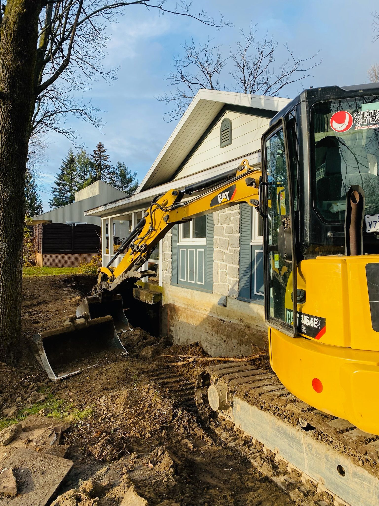 Une excavatrice jaune creuse un trou devant une maison.