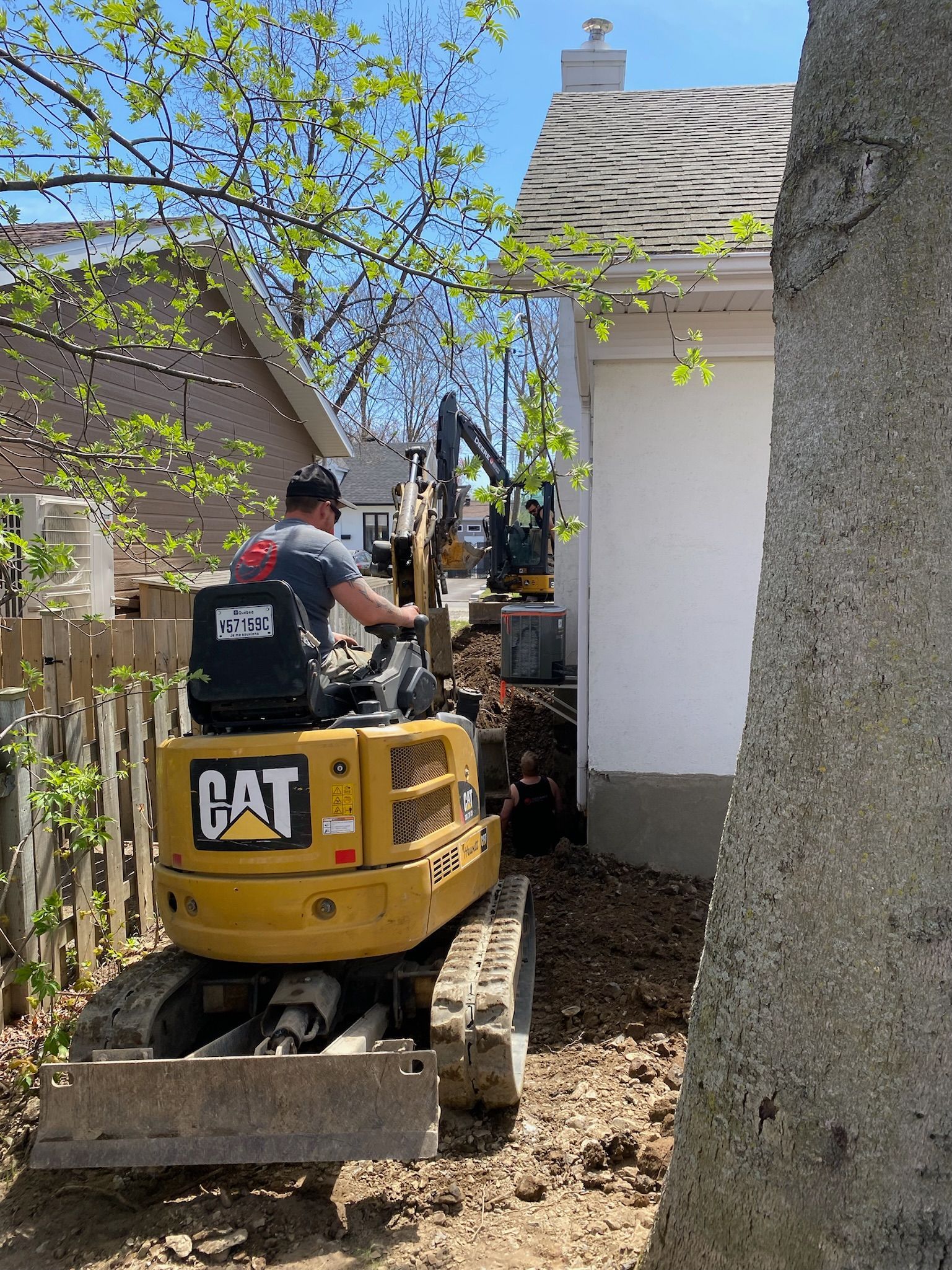 Un homme conduit une excavatrice à chat devant une maison.