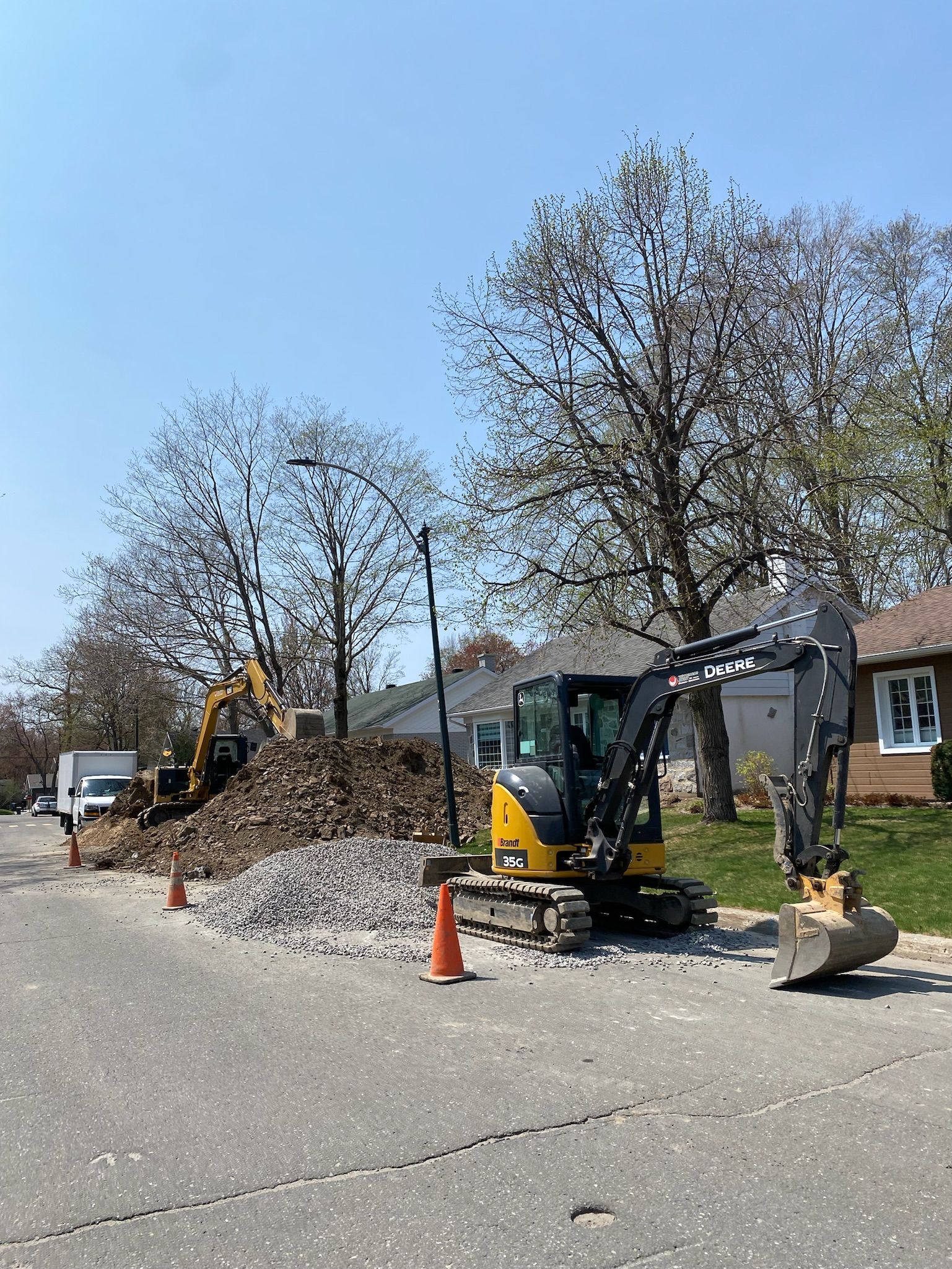 Une excavatrice jaune et noire est assise sur le bord d'une route à côté d'une maison.